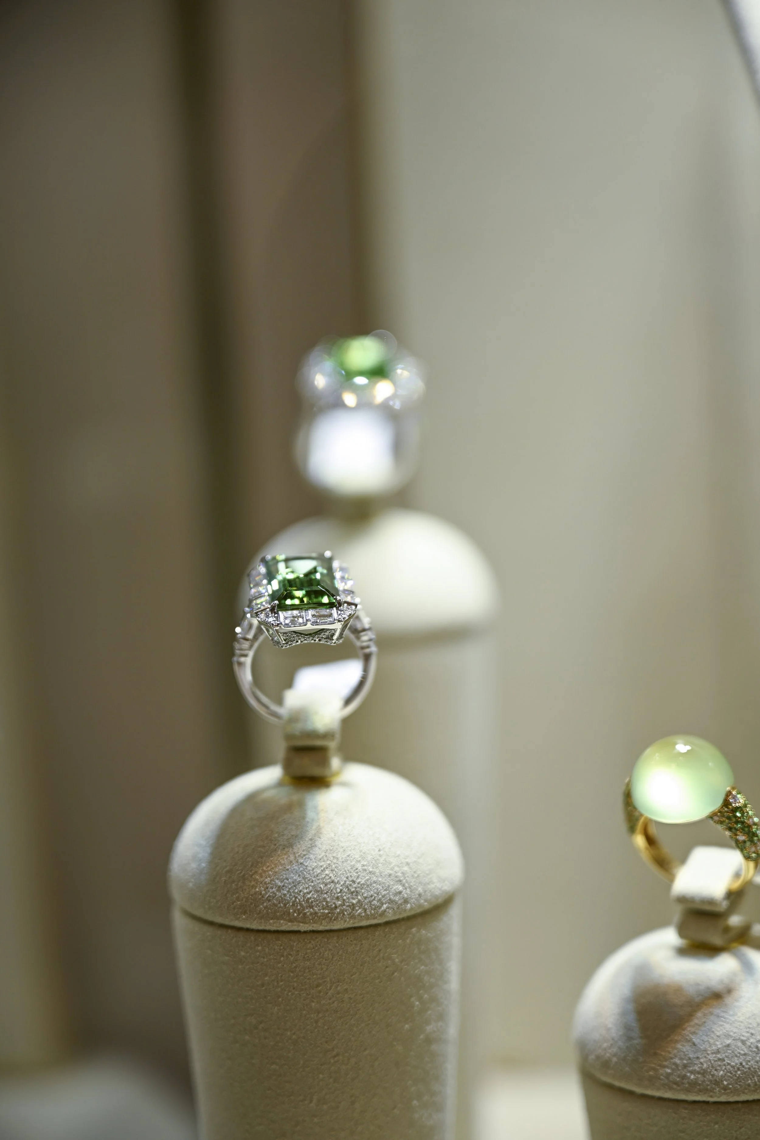 Close-up of display jewelry including a ring with a green gemstone and surrounding diamonds, placed on a jewelry stand.