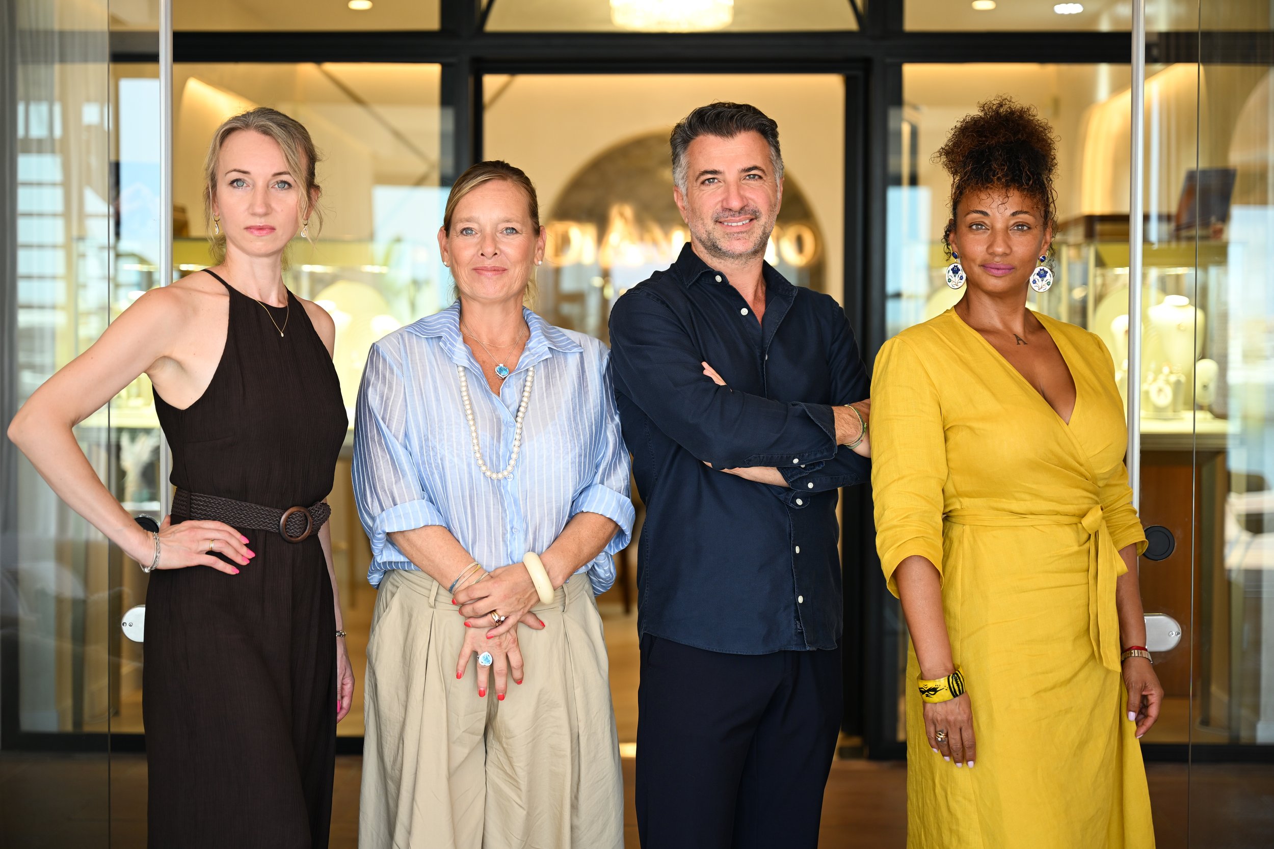 A diverse group of four people that is the team of diamotto , three women and one man, standing together in front of a glass entrance with a modern, well-lit interior in the background. Professionals working with diamons and jewellery in Mallorca