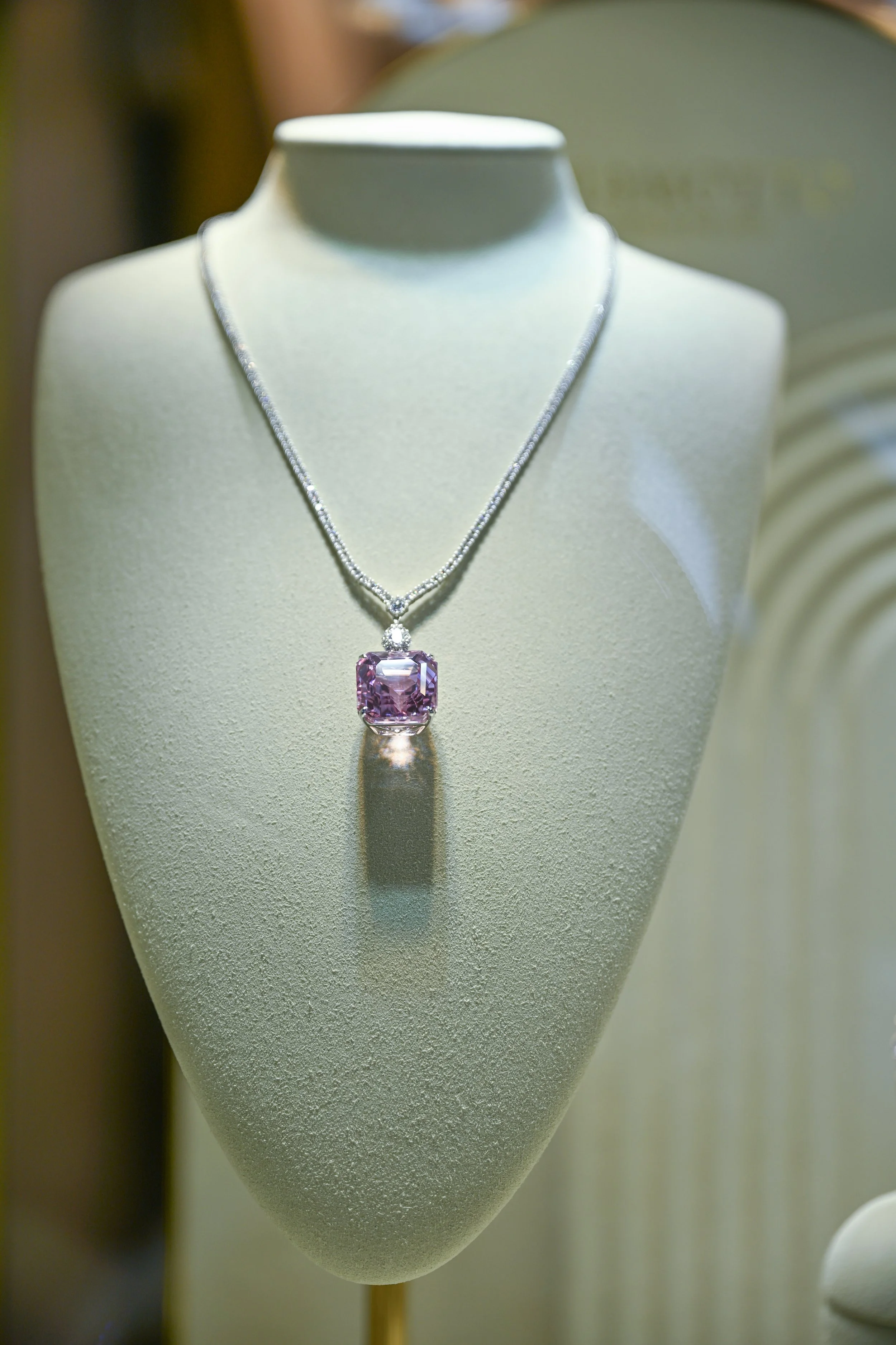 Display of a silver necklace with a large, pink gemstone pendant on a mannequin bust.