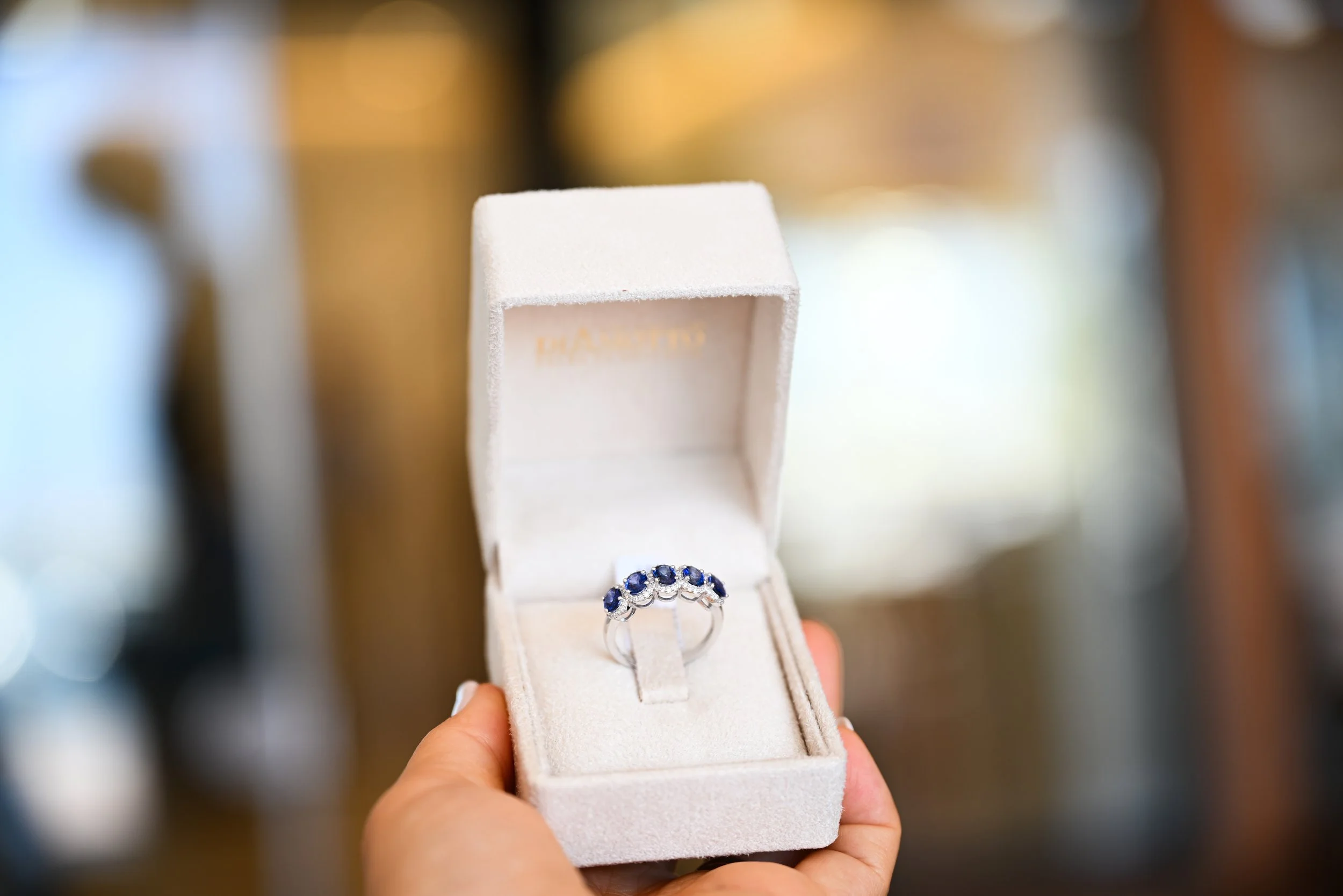 A person holding a jewelry box with a ring featuring multiple blue stones inside.