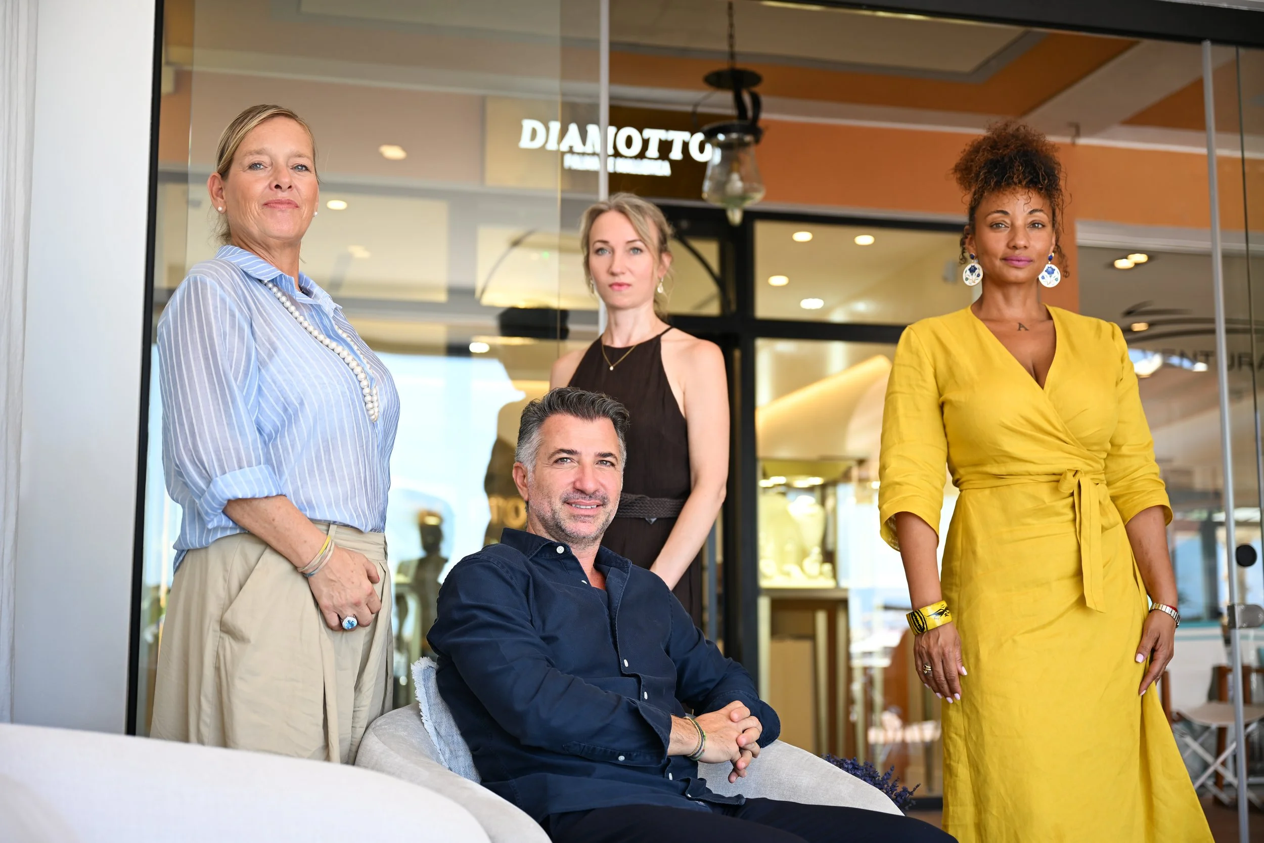 Four diverse adults, two women and two men, posing in and outside of a modern building with a glass door, during daytime.