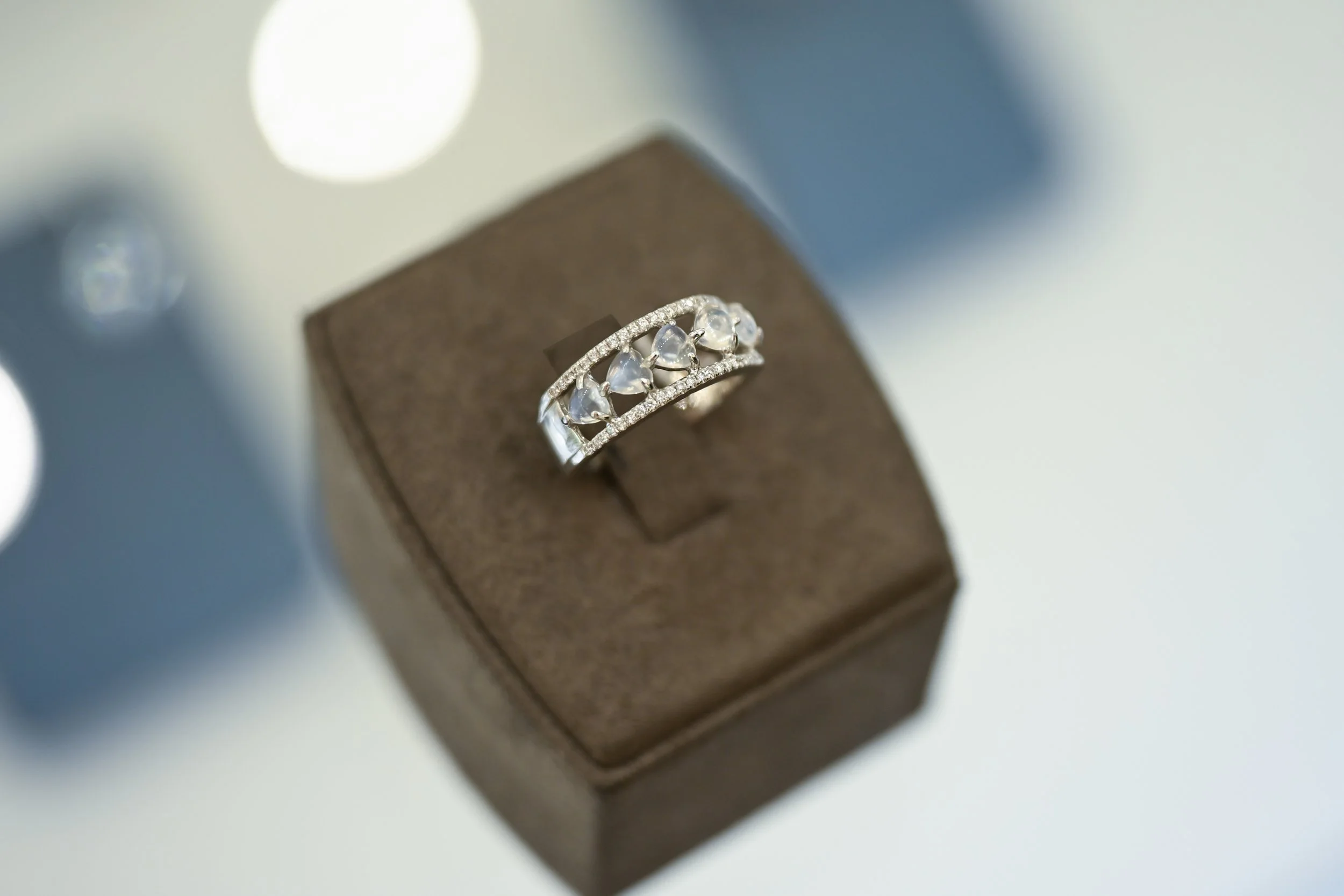 Close-up of a silver ring with heart-shaped gemstones on a brown jewelry display stand.