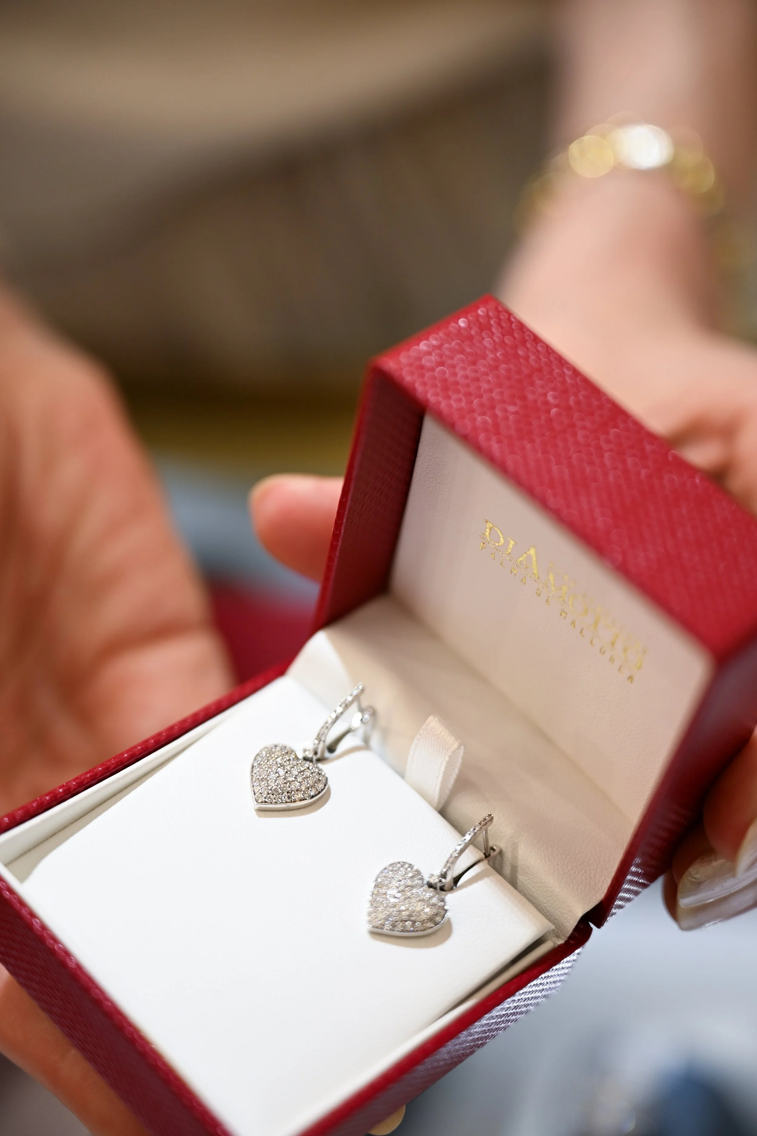 A red jewelry box containing a heart-shaped diamond pendant and matching earrings with diamonds, inside a white interior.