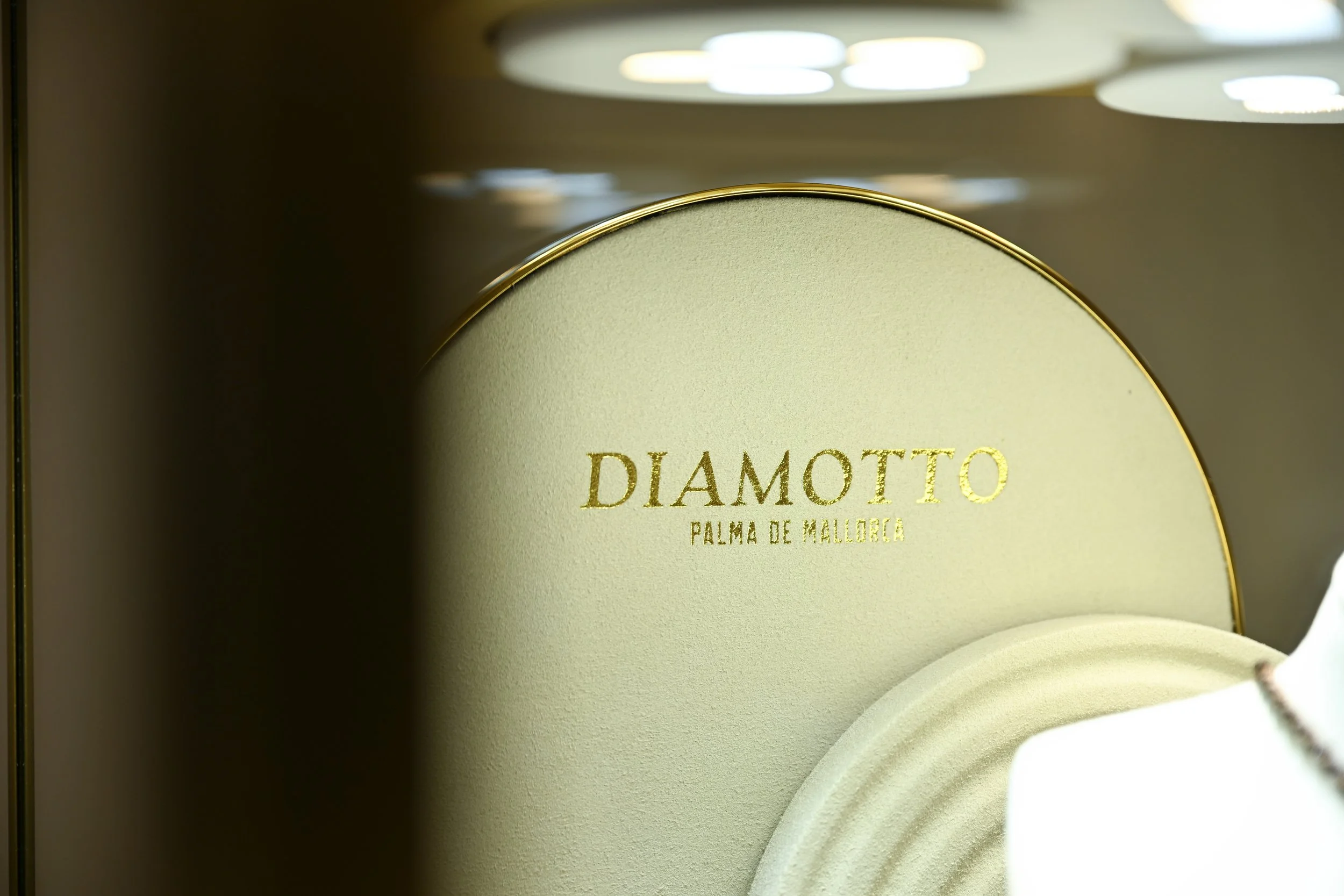Close-up of a jewelry box displaying a gold ring with the word 'DIAMOND' and 'PALMA DE MALLORCA' written on the inside of the lid, with a blurred background of jewelry or other items.