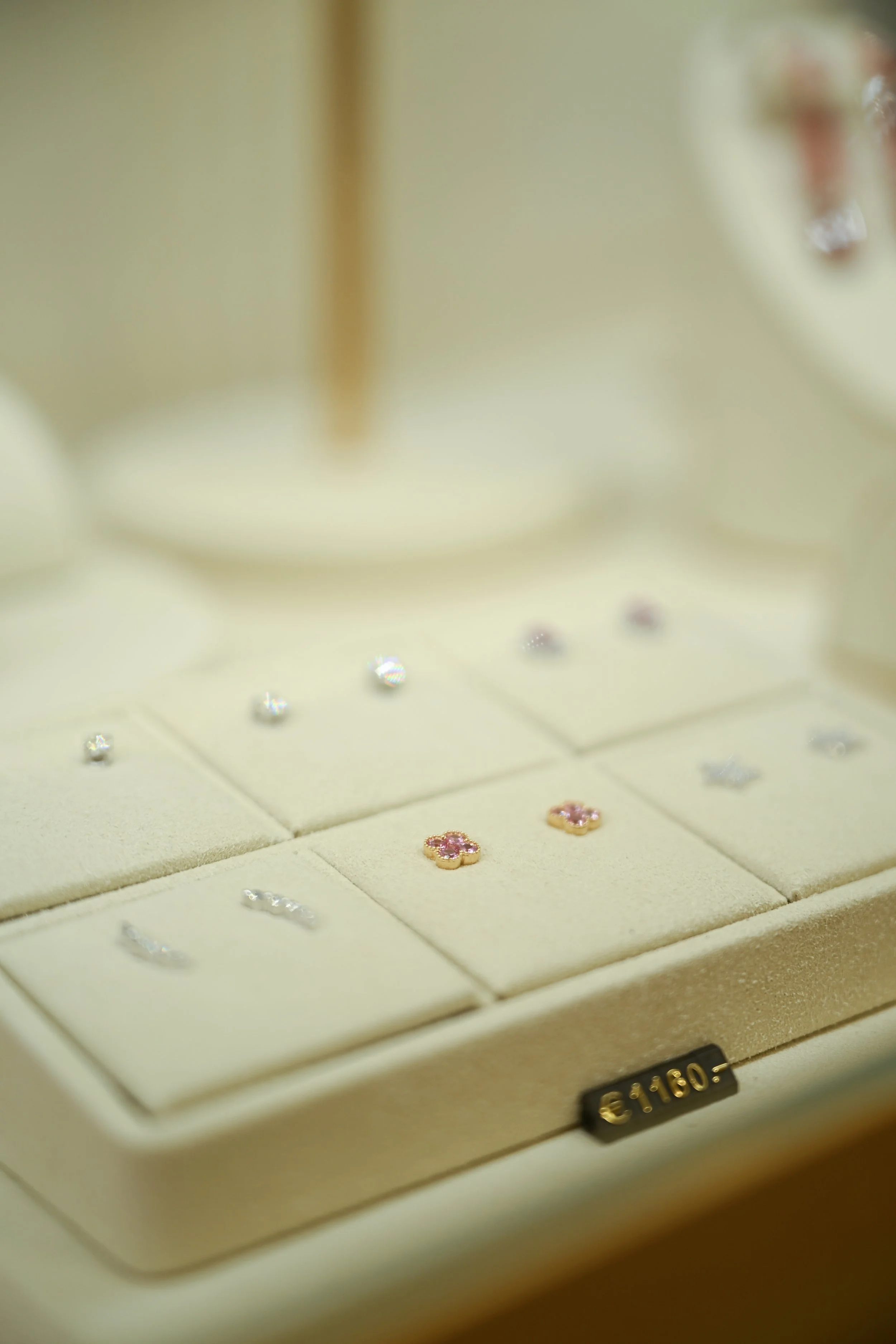 Close-up of a jewelry display tray with small pink and clear gemstone earrings and flower-shaped jewelry with pink stones.