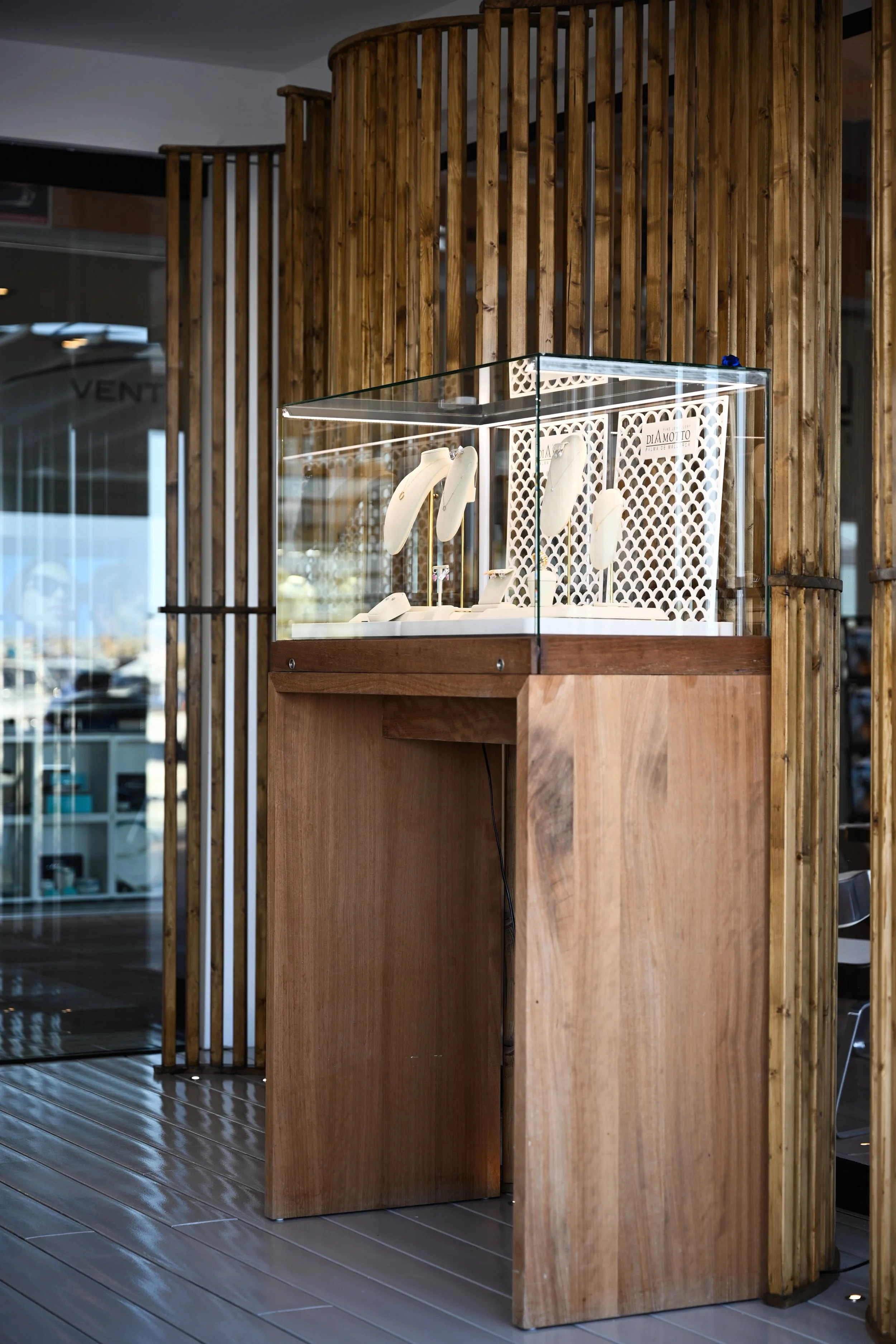 Display case with jewelry inside on a wooden stand in front of a wooden slatted decorative wall, with a restaurant or shop interior visible in the background.