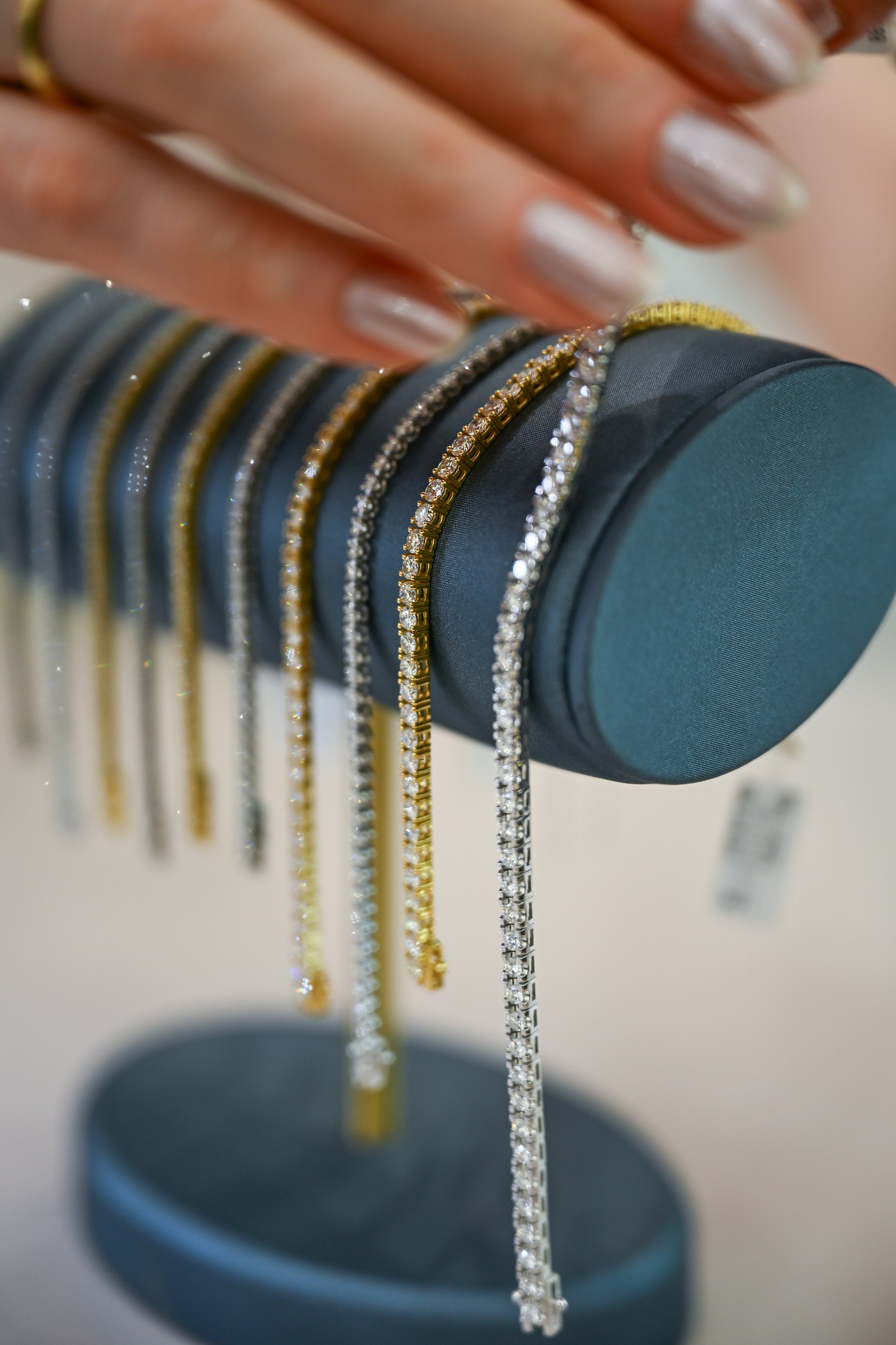 Close-up of various gold and silver jewelry necklaces displayed on a dark cylindrical stand.