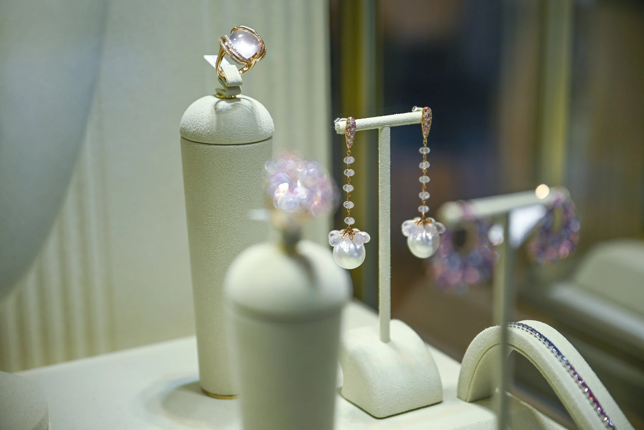 Display of jewelry including a pearl ring, earrings with white stones and pink accents, and a bracelet with white stones, all arranged on a jewelry display stand. At diamotto in mallorca