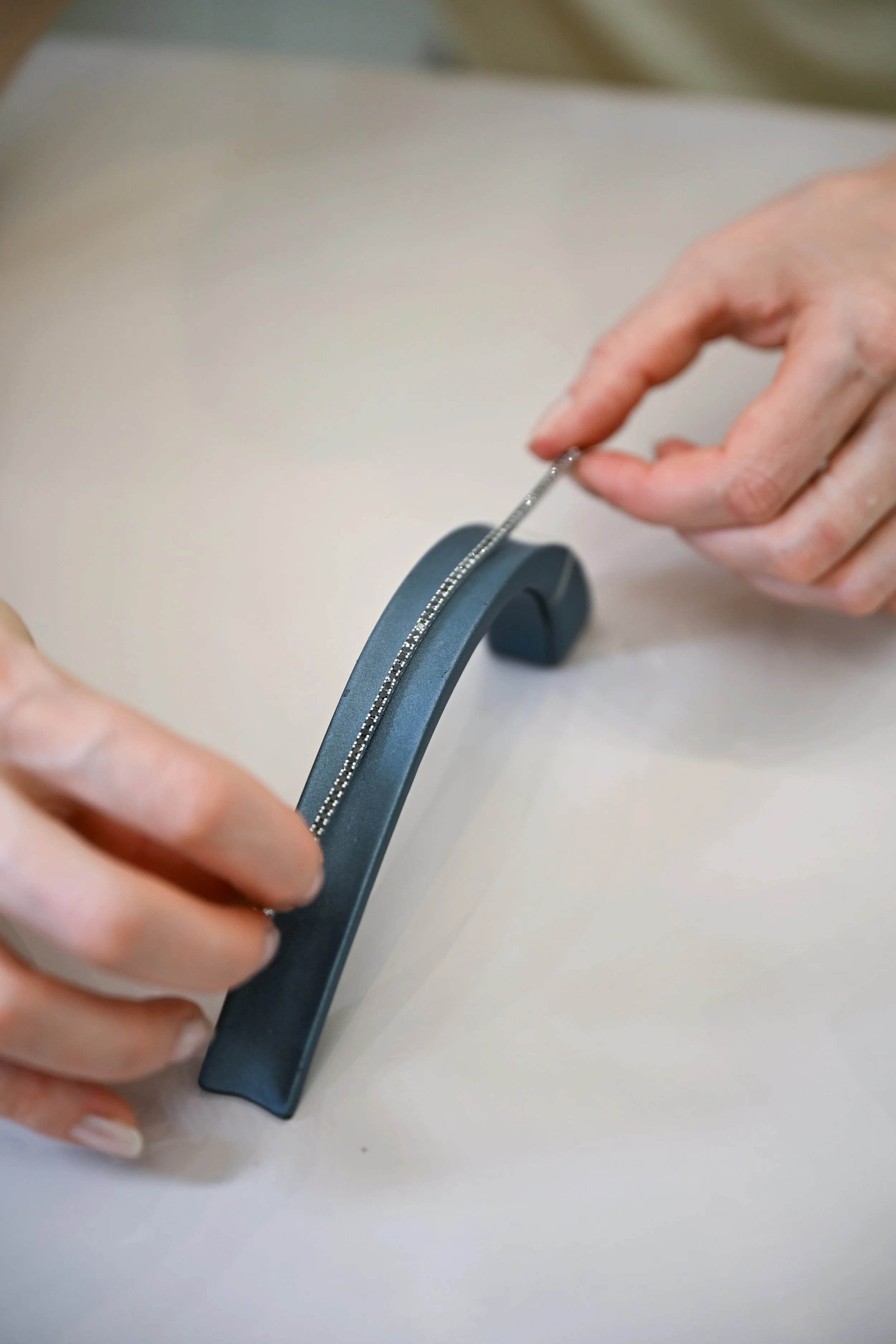 A person's hand using a small tool to attach or adjust a zipper on a blue fabric item, possibly clothing or a bag, on a light-colored surface.