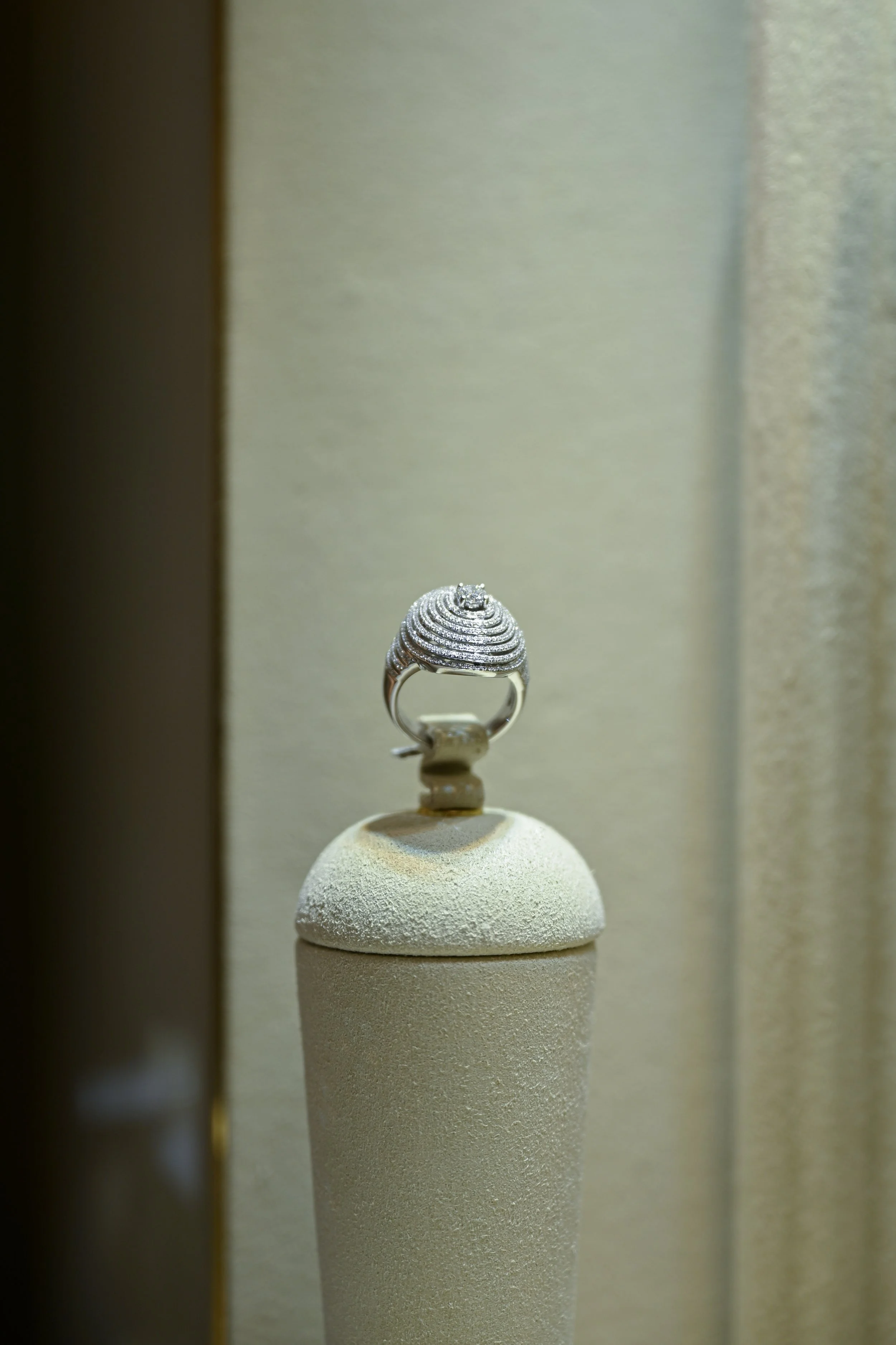 A silver ring with a large central diamond and smaller diamonds on the band displayed on a white stand.