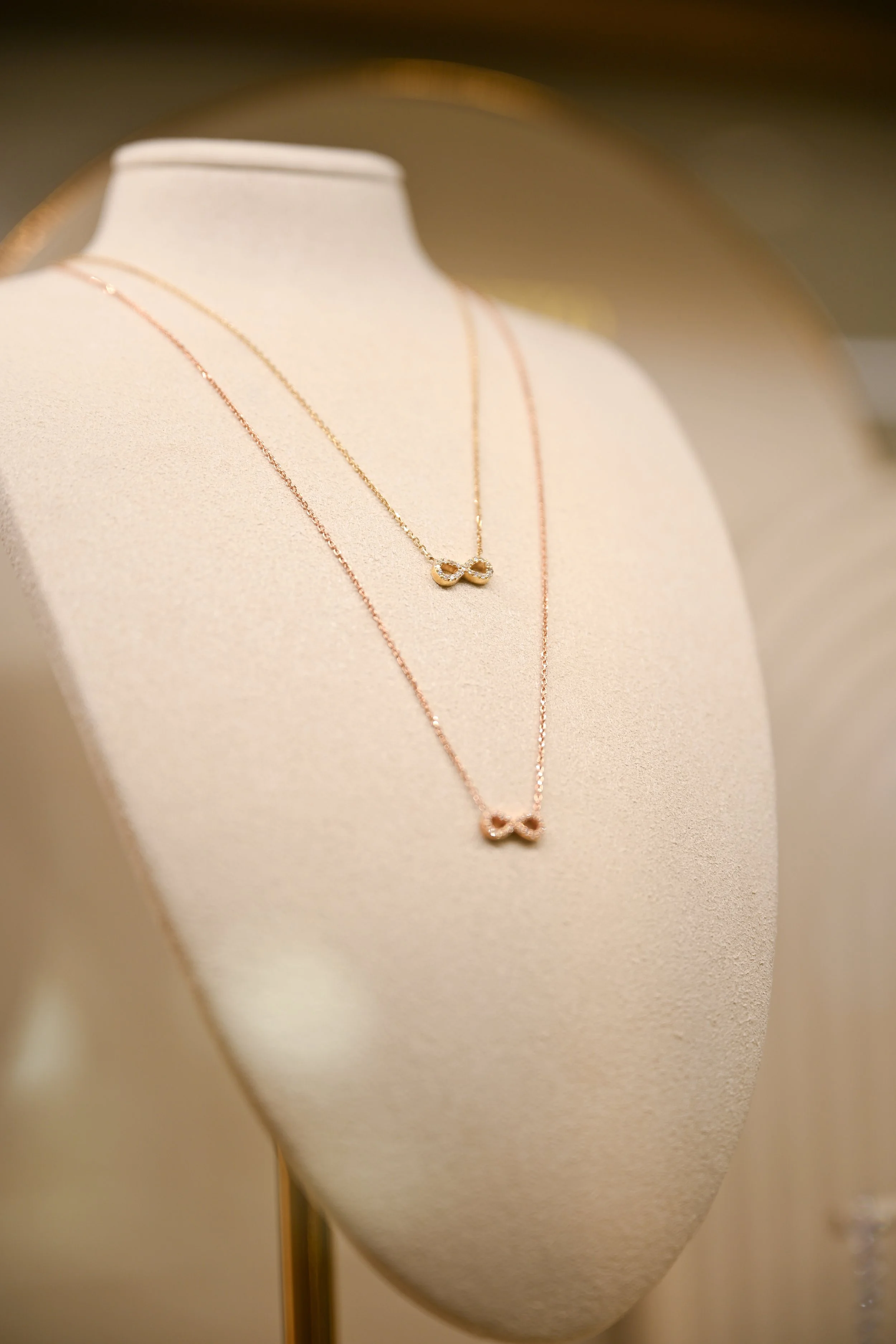 Close-up of a jewelry display featuring a gold necklace with an infinity symbol pendant on a beige mannequin bust.