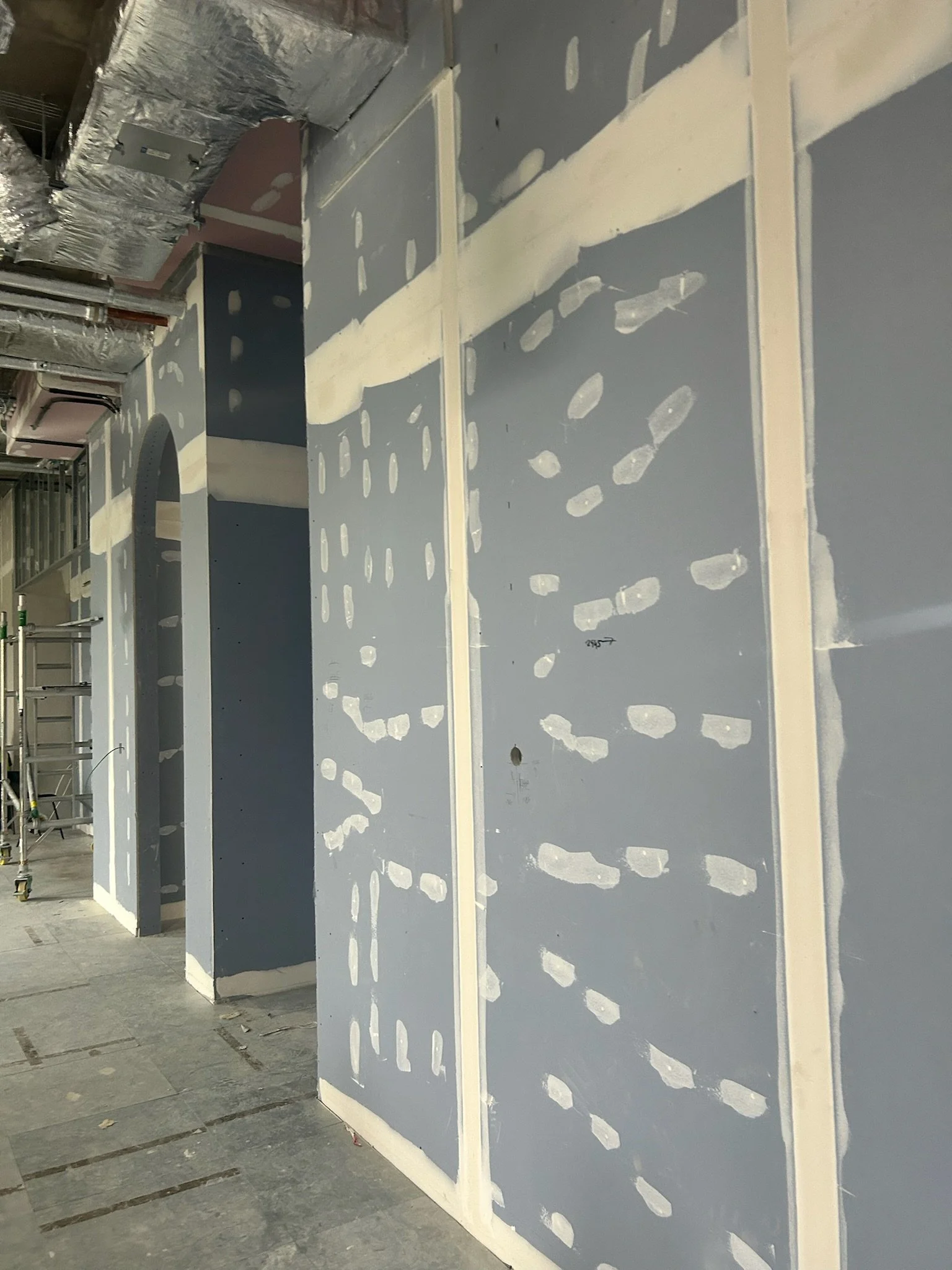 Construction or renovation site with drywall panels and insulation, showing drywall patches and unfinished wall surfaces.