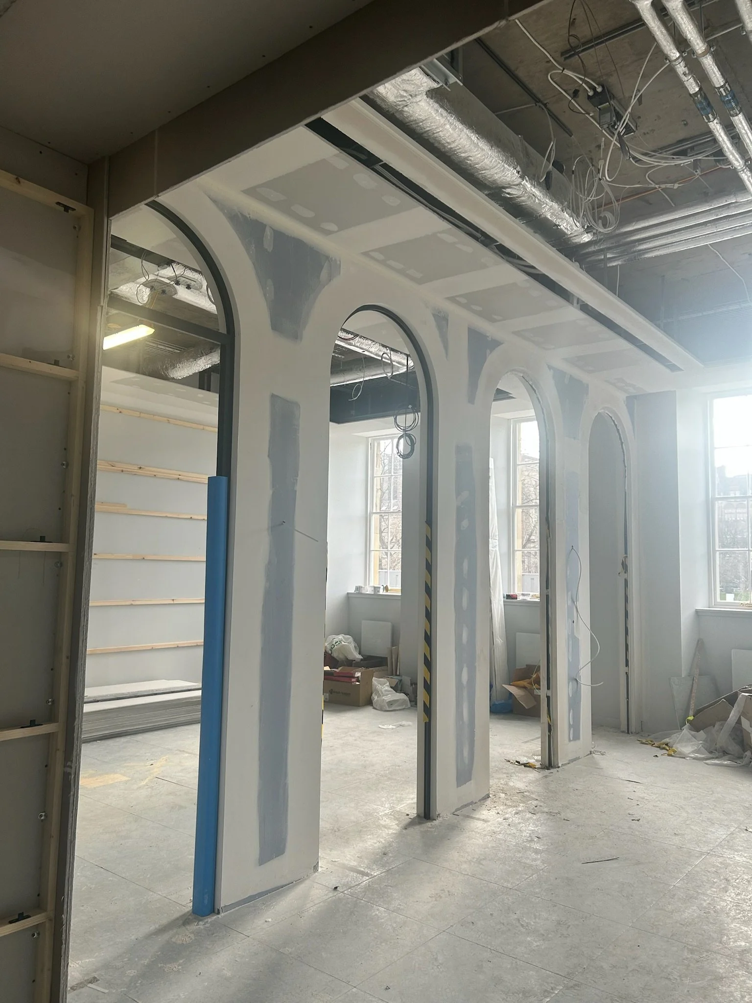 Interior of a building under construction with unfinished walls, exposed pipes, and construction materials scattered on the floor.