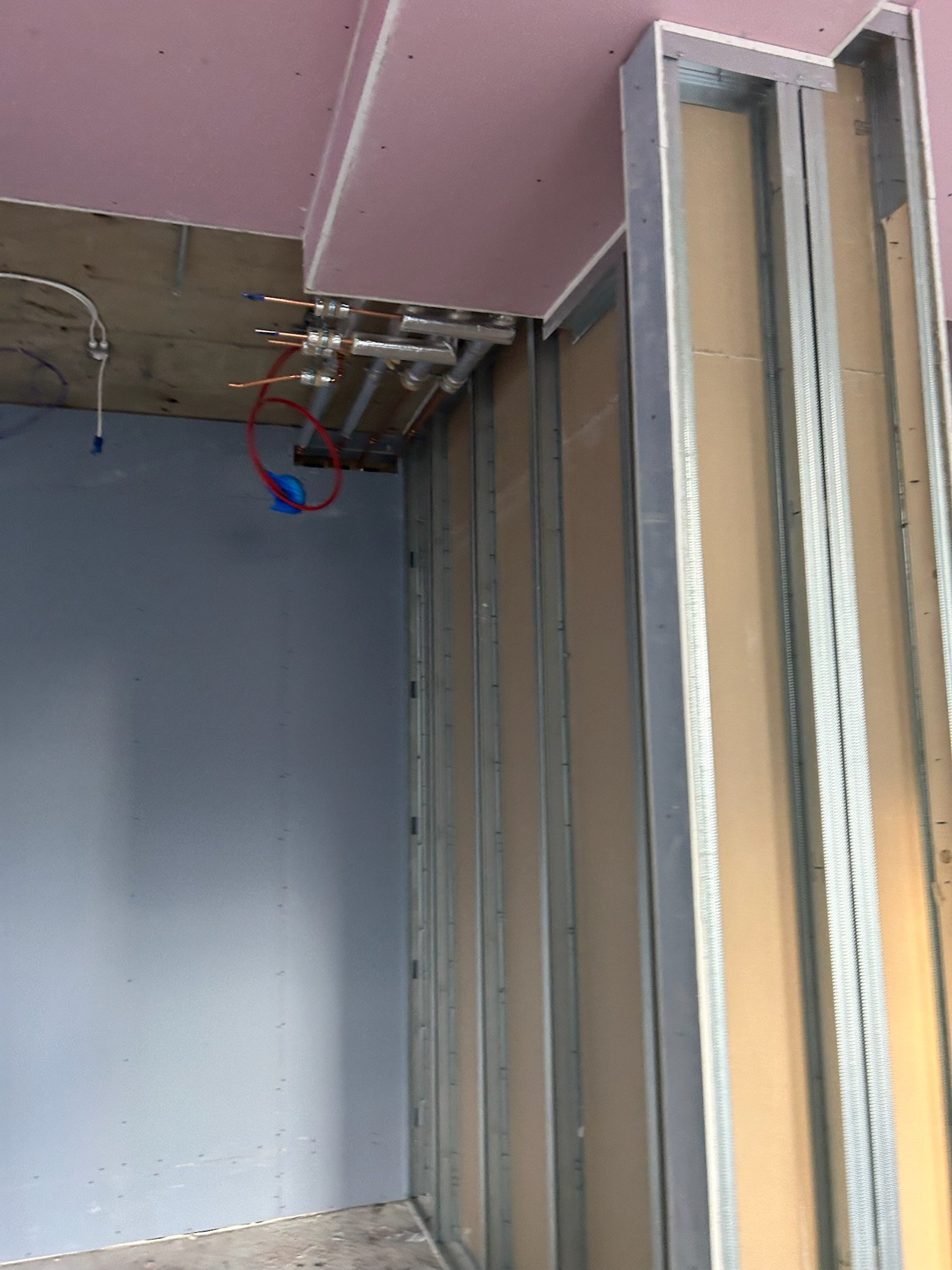 Construction site with metal framing, pipes, and pink drywall in an unfinished room.