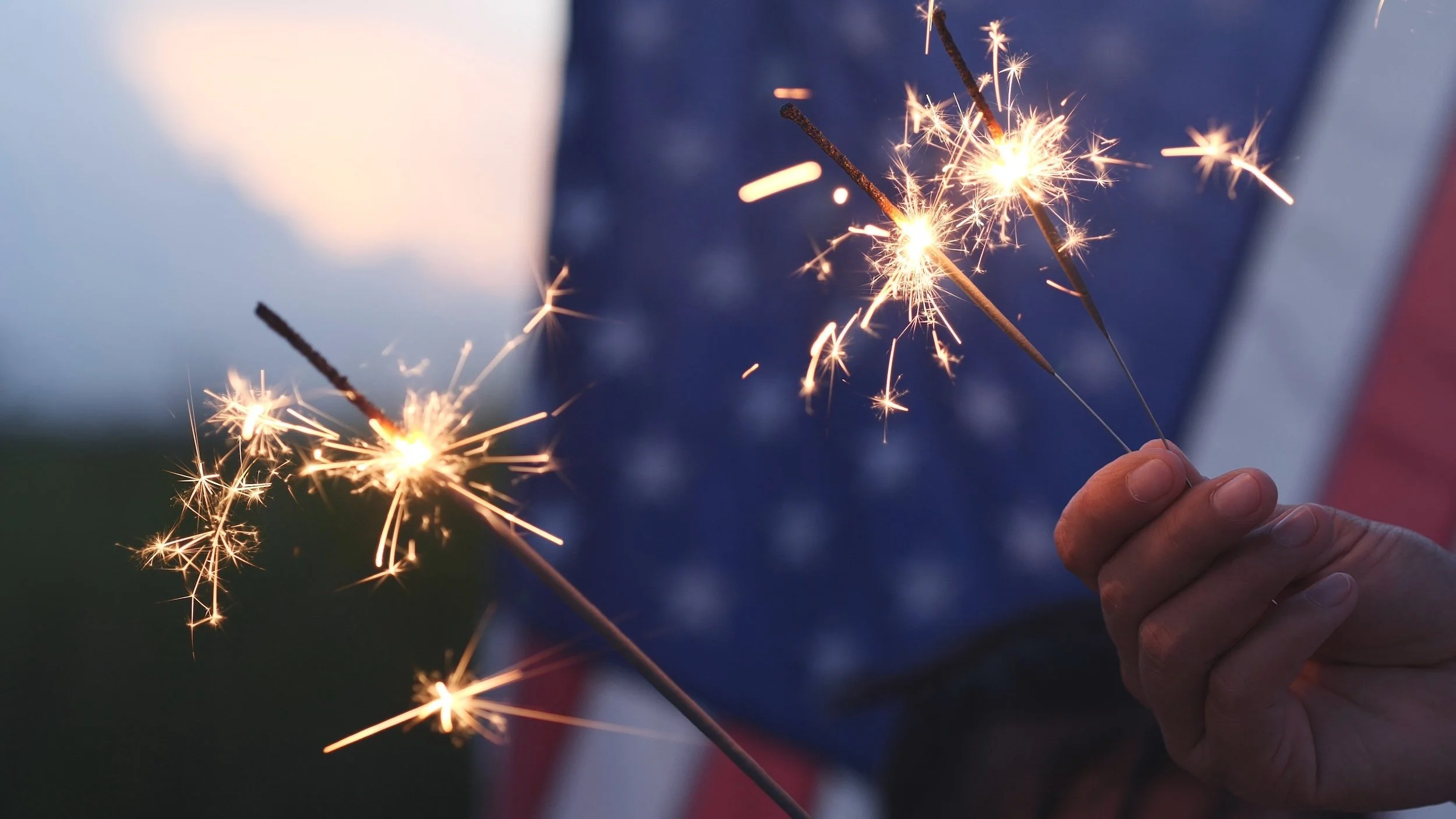 hands holding sparklers in front of an american flag