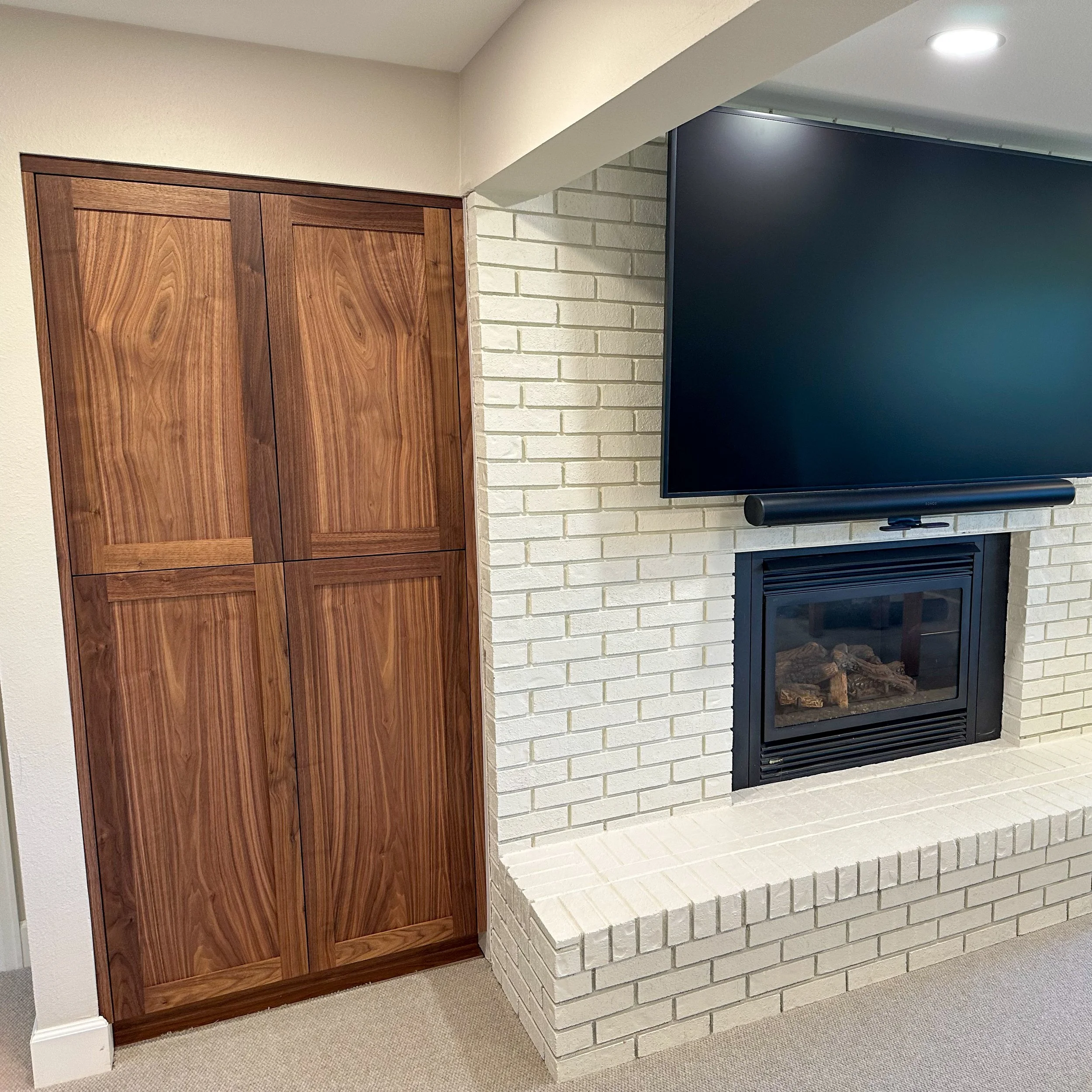 A living room corner with a closed wooden closet, a white brick fireplace, and a mounted flat-screen TV with a soundbar underneath.