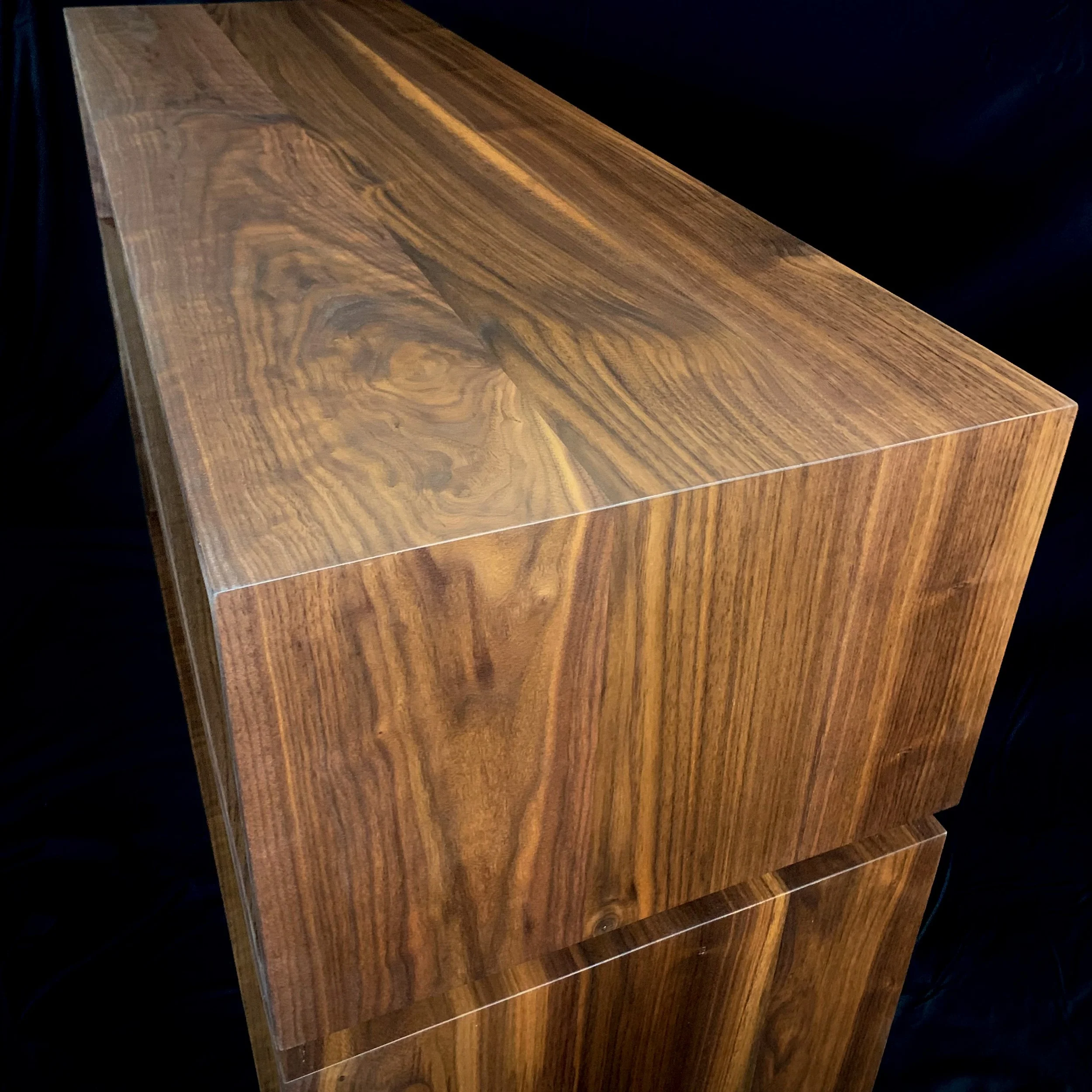 A polished wooden cube with natural wood grain patterns, set against a black background.