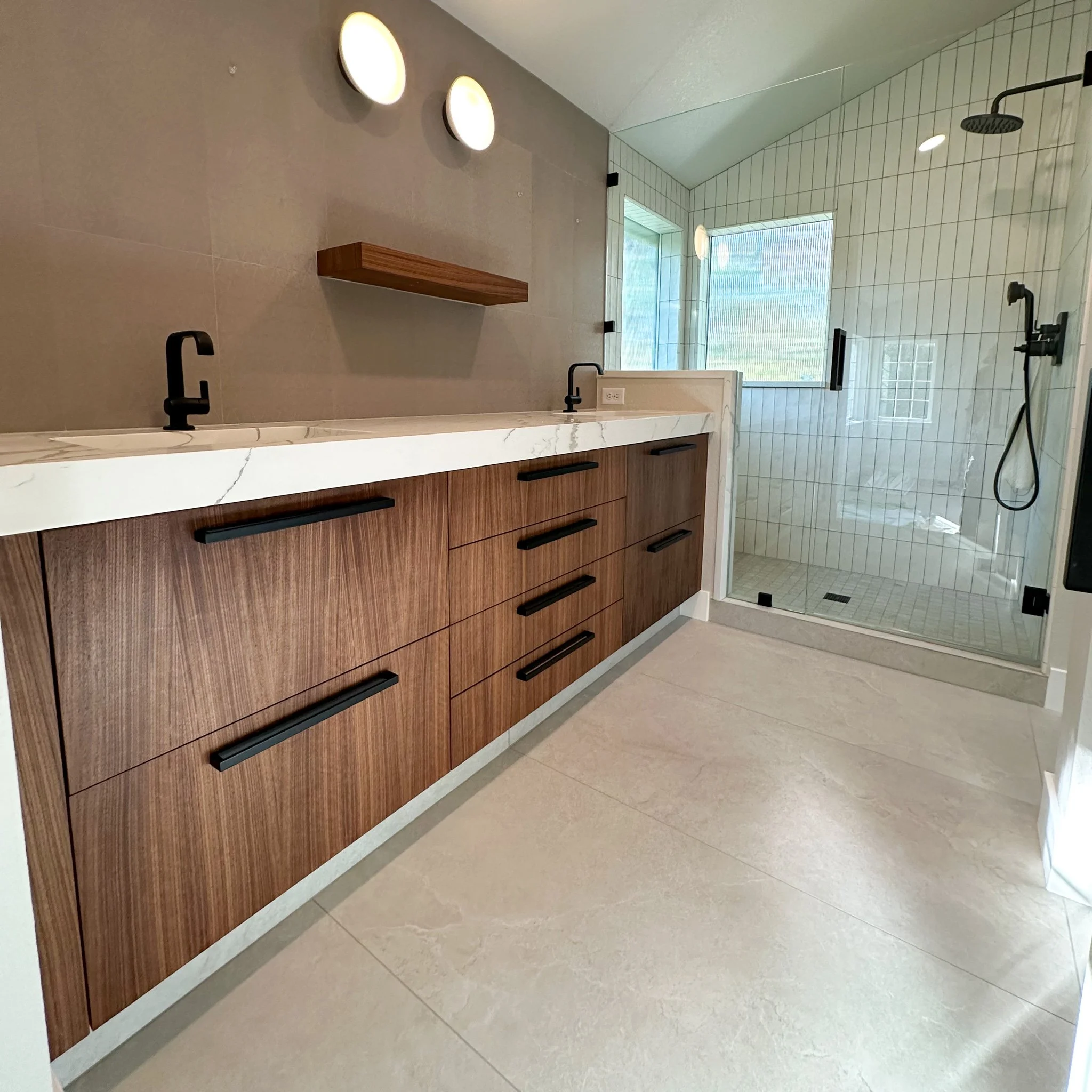 Modern bathroom with a wooden vanity, white marble countertop, black faucets, and a glass-enclosed shower with tiled walls and a rainfall showerhead.