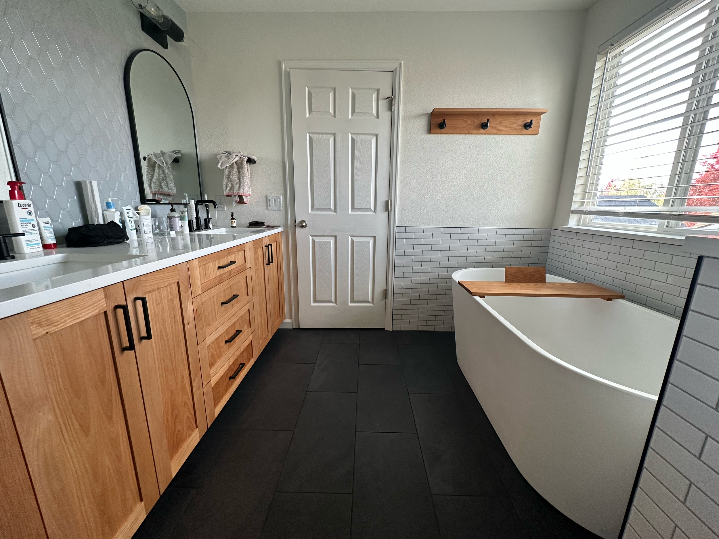 Modern kitchen with white walls, gray subway tile backsplash, wooden cabinets, white hex tile floor, window with blinds, and a white range hood.
