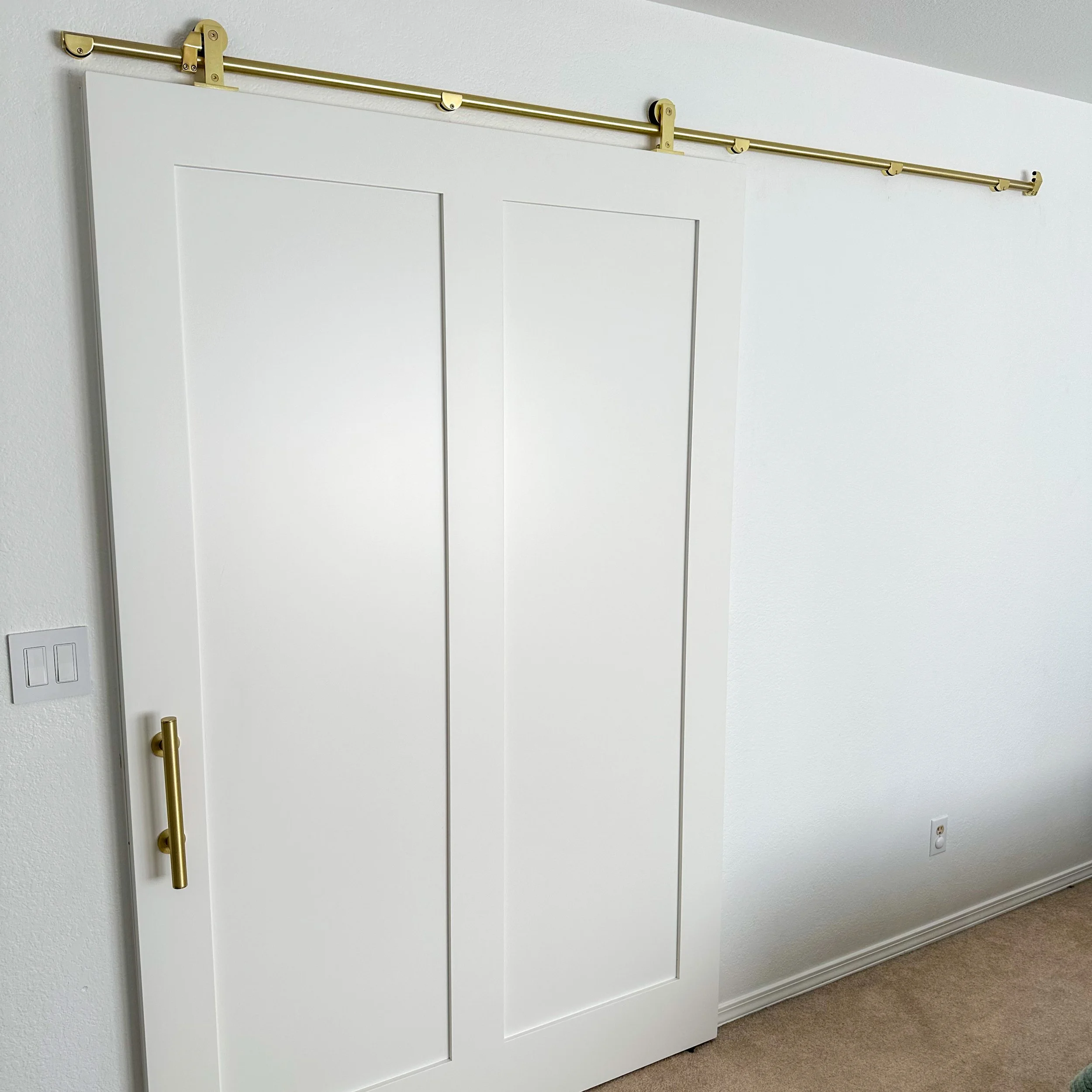 A white sliding door closet with gold hardware and track system, situated in a room with white walls and beige carpet.