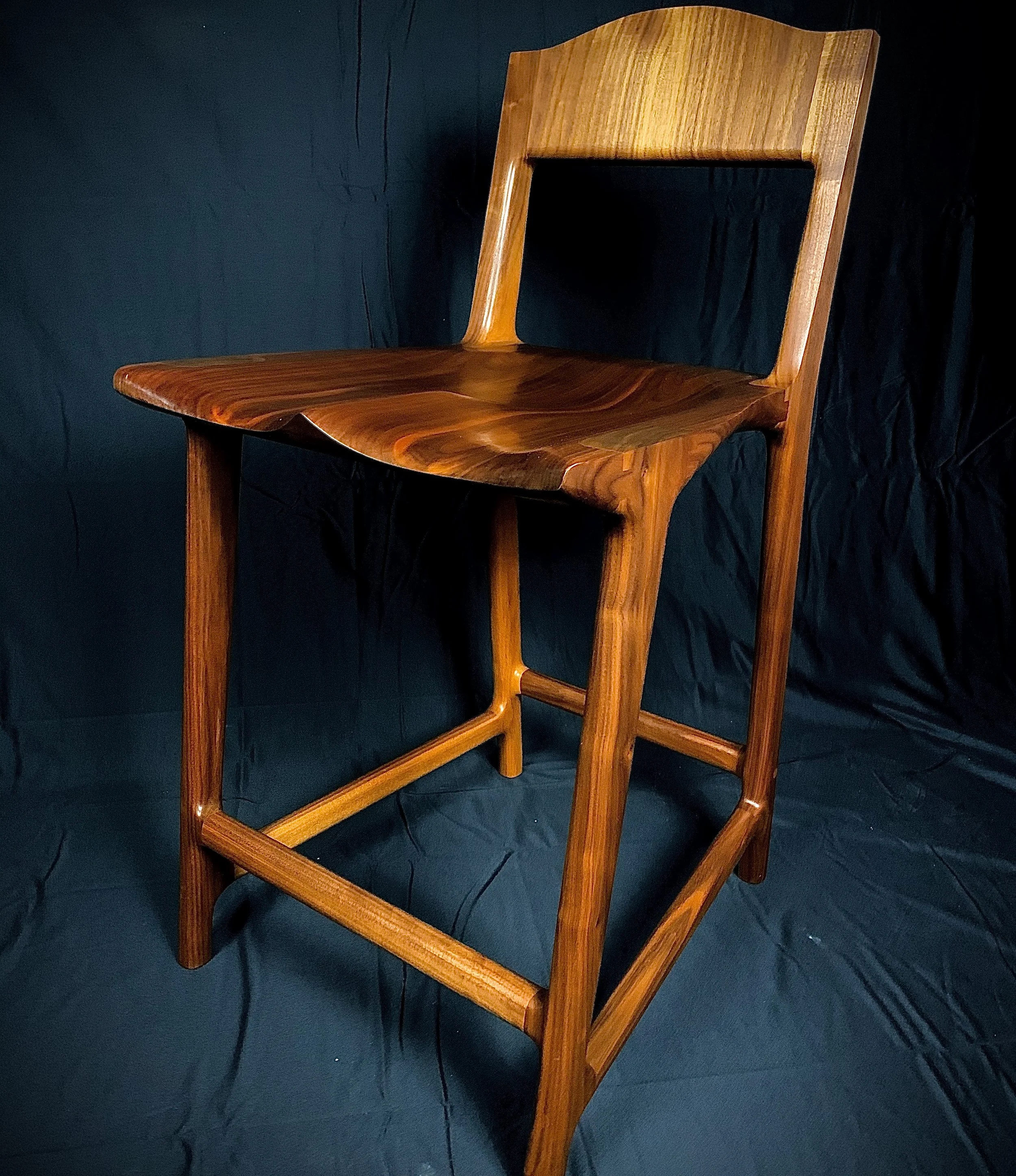 A wooden chair with a curved backrest and a shiny polished seat, set against a dark background.