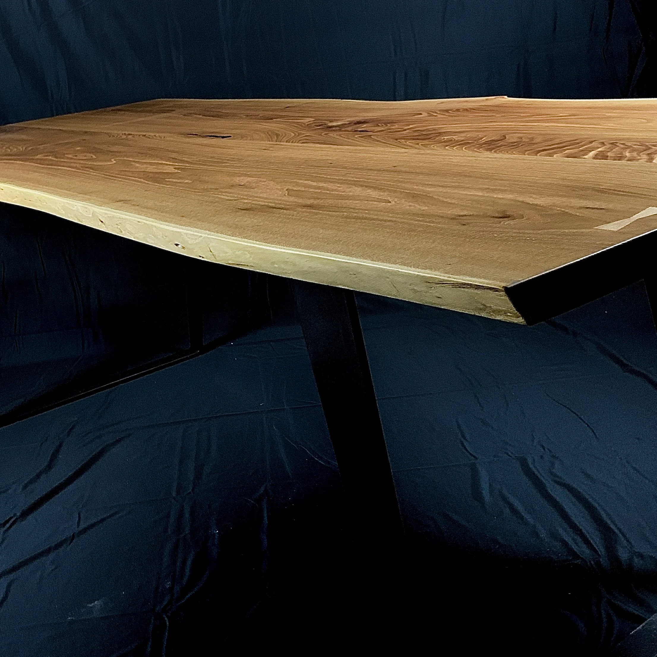 A wooden tabletop with a natural finish, supported by black legs, against a dark background.