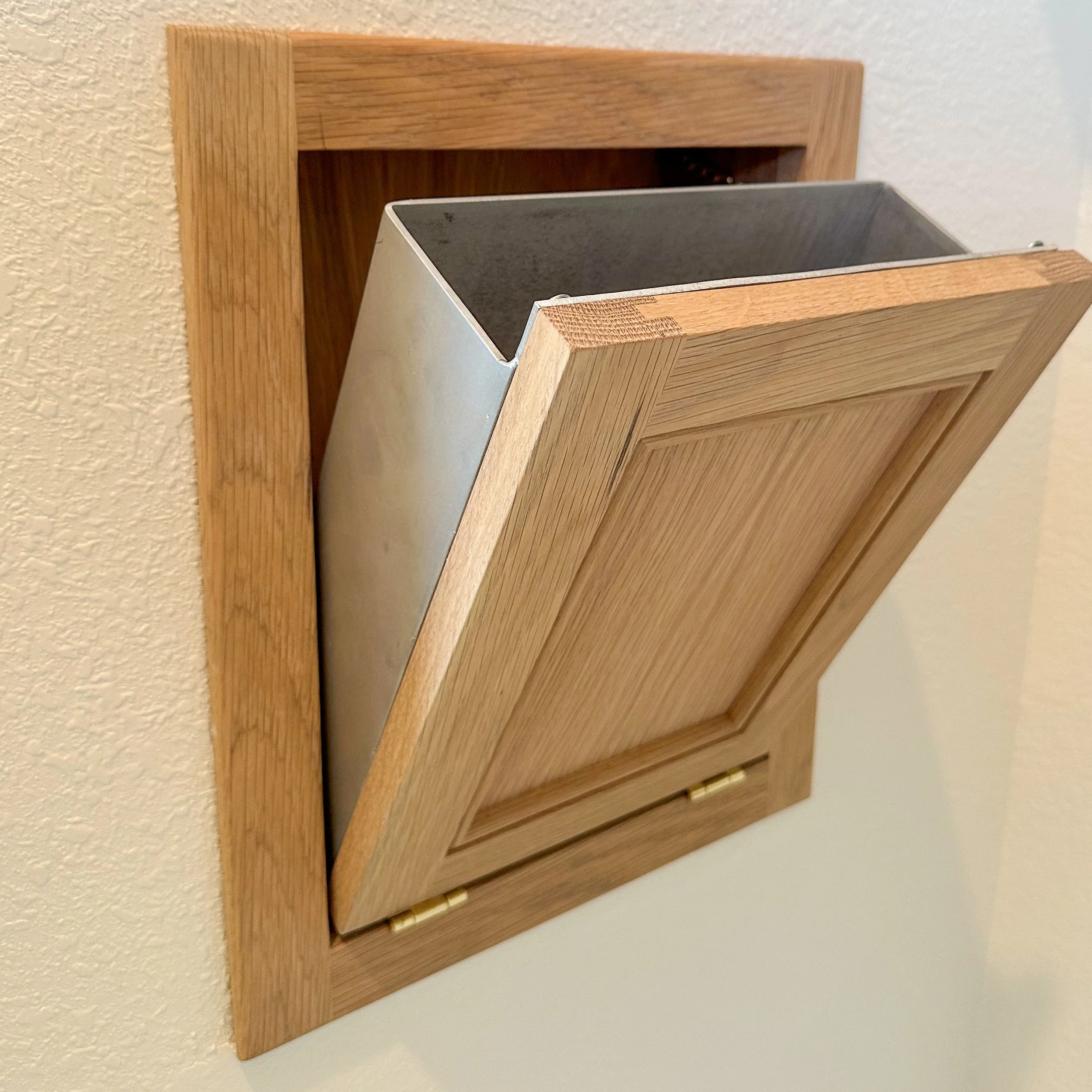A wooden wall-mounted mailbox with a slanted lid, partially open to reveal a metal lining inside.