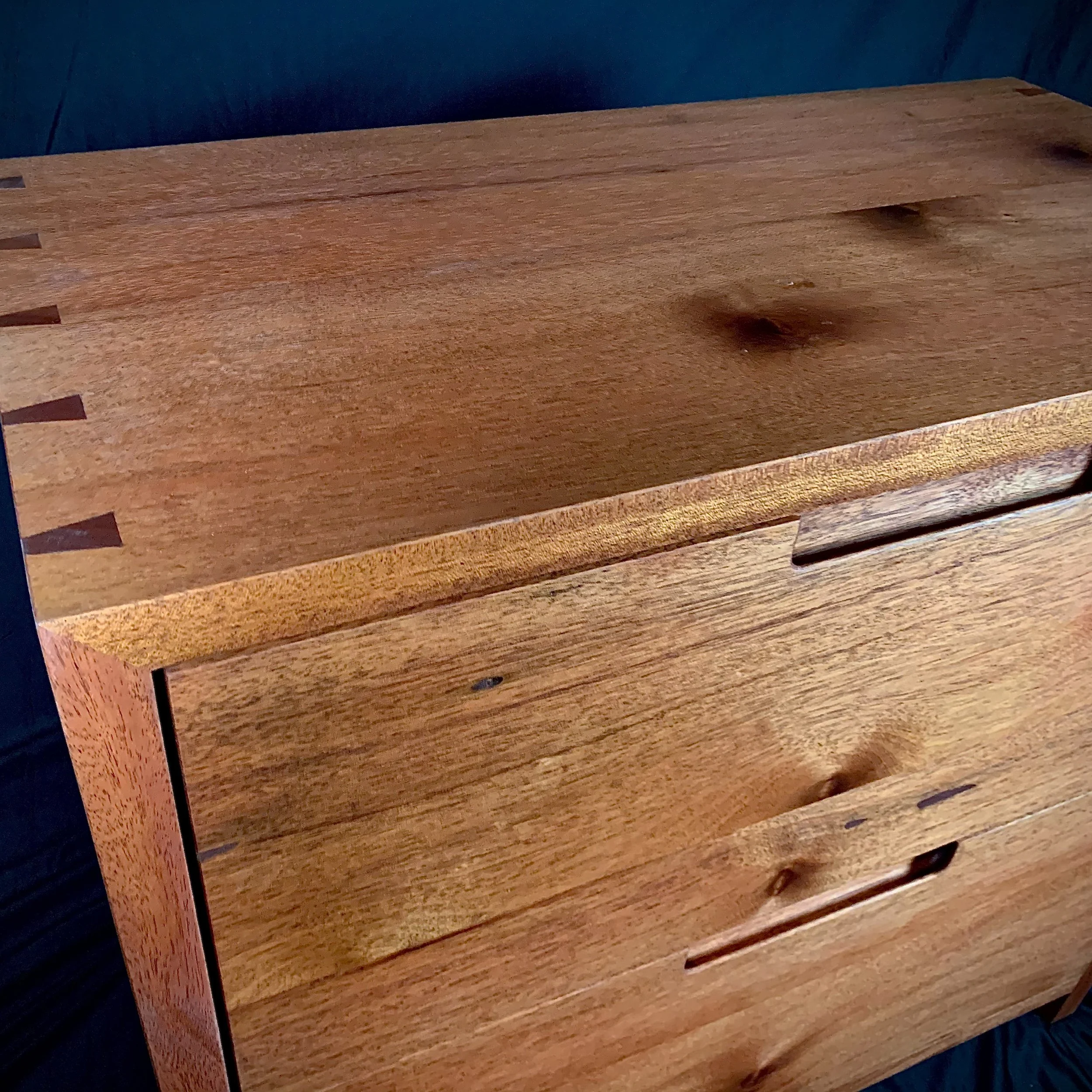 Close-up of a wooden dresser with a natural finish and visible wood grain, featuring three drawers with cutout handles.