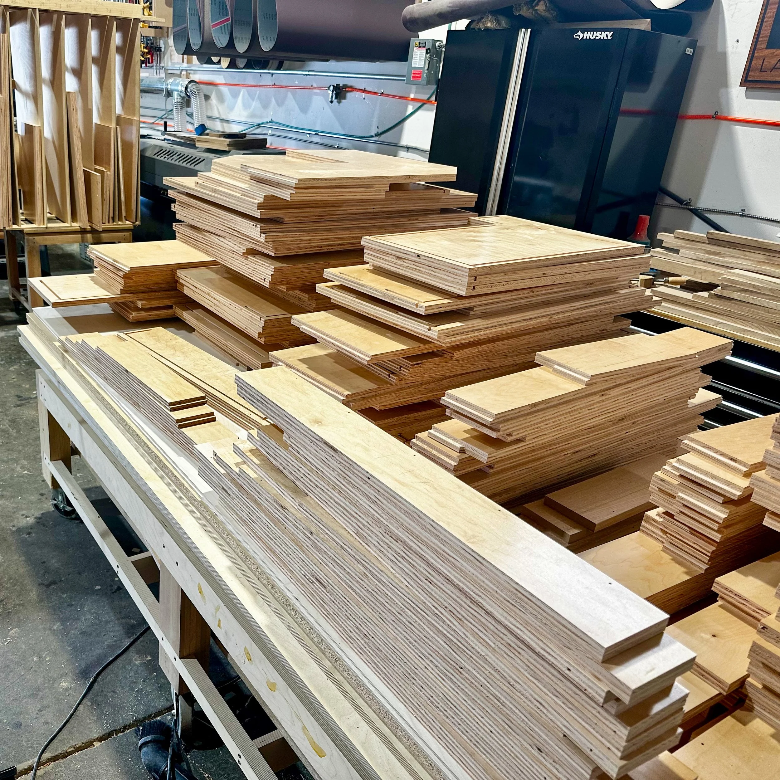 Stacks of unfinished wooden boards and pieces arranged on a work table in a woodworking shop.