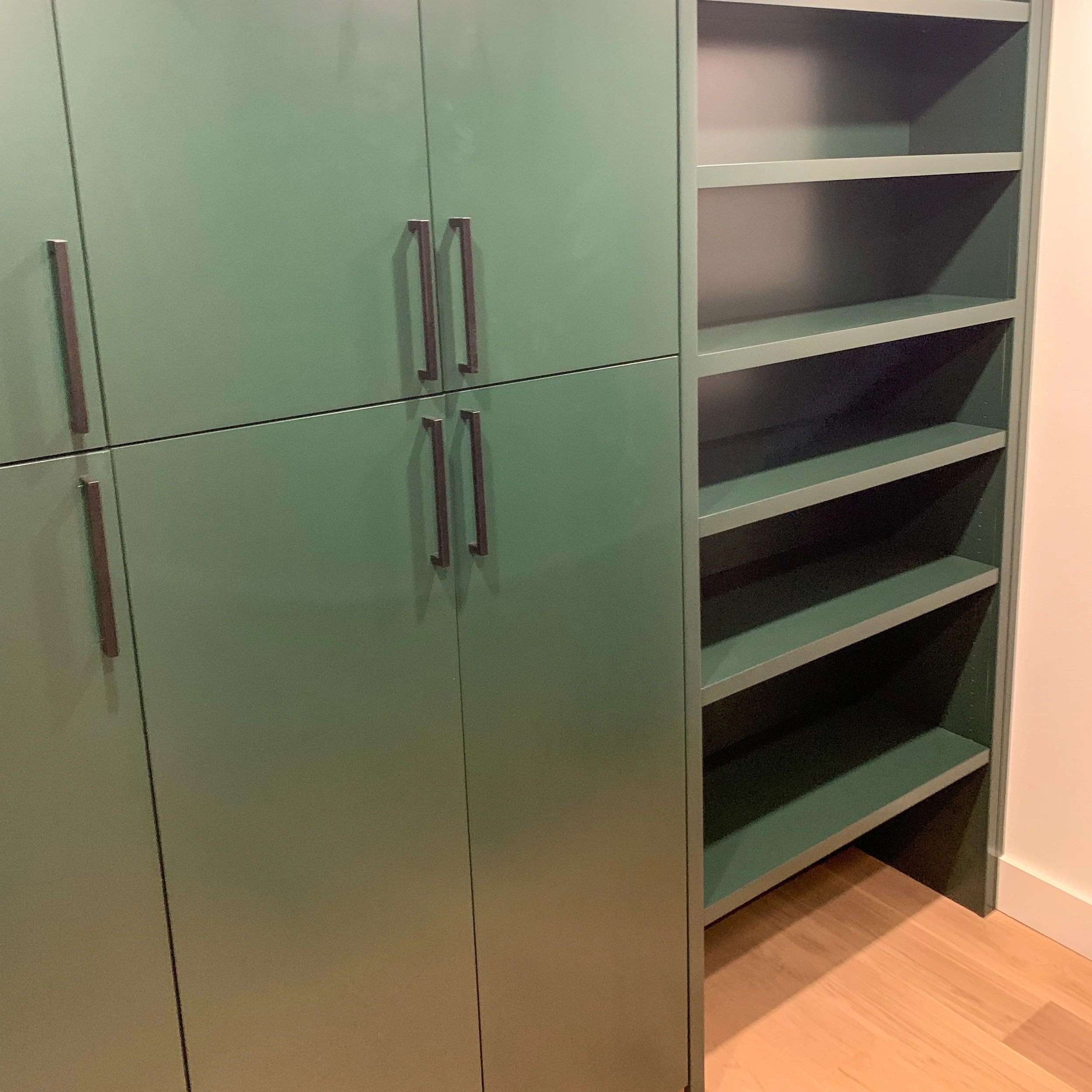 Green kitchen cabinets with black handles and open shelving unit with four empty shelves on a wooden floor.