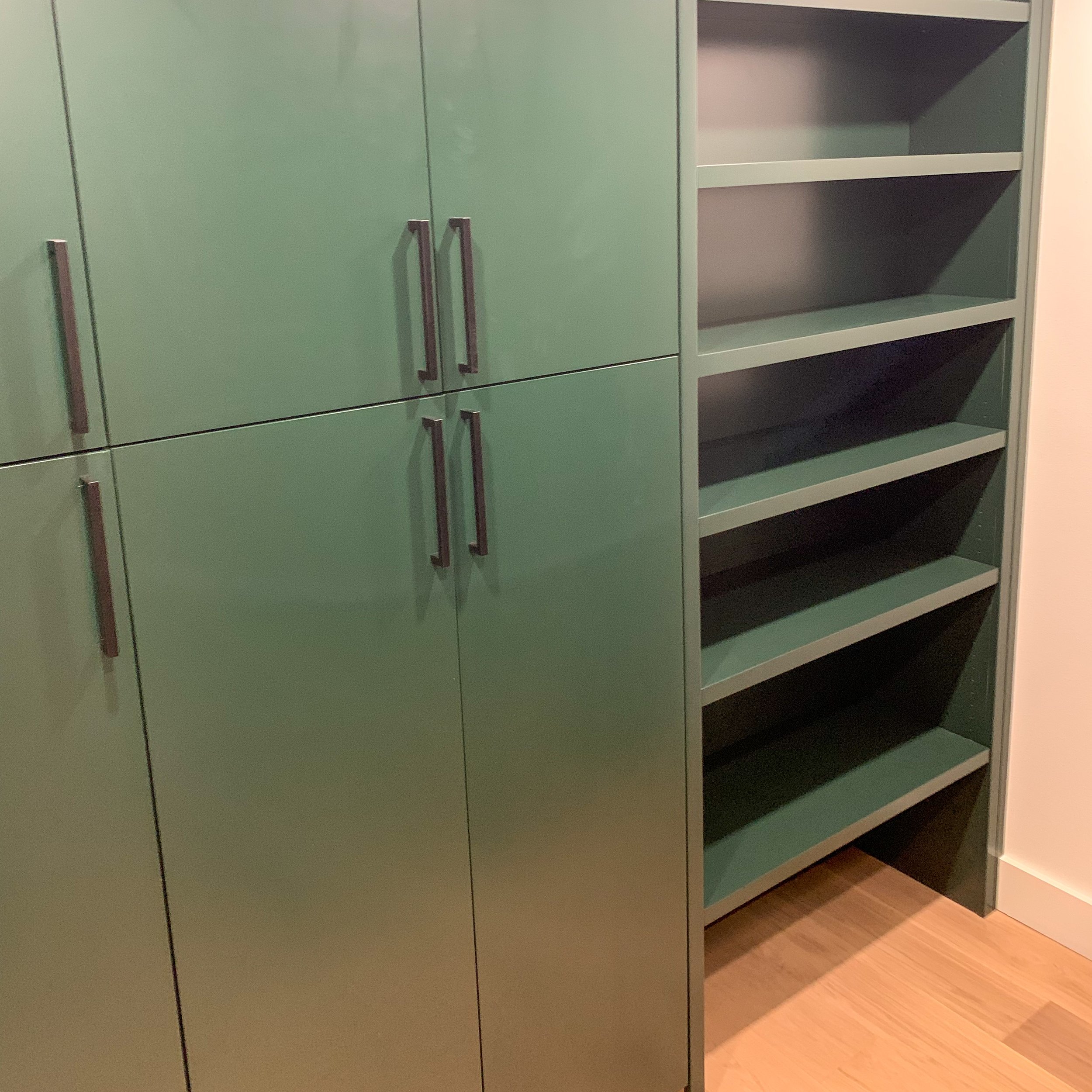 Green kitchen cabinets with silver handles and open shelving on the right side, with a wooden floor beneath.