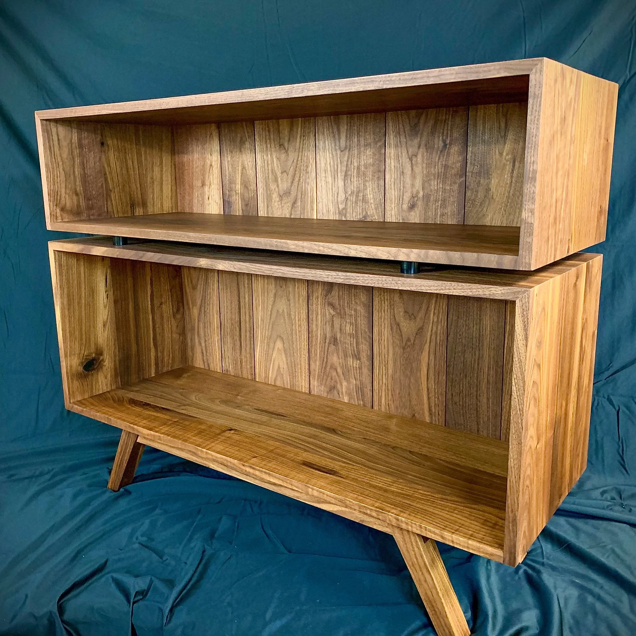 A wooden bookshelf with two open compartments, standing on four angled legs.