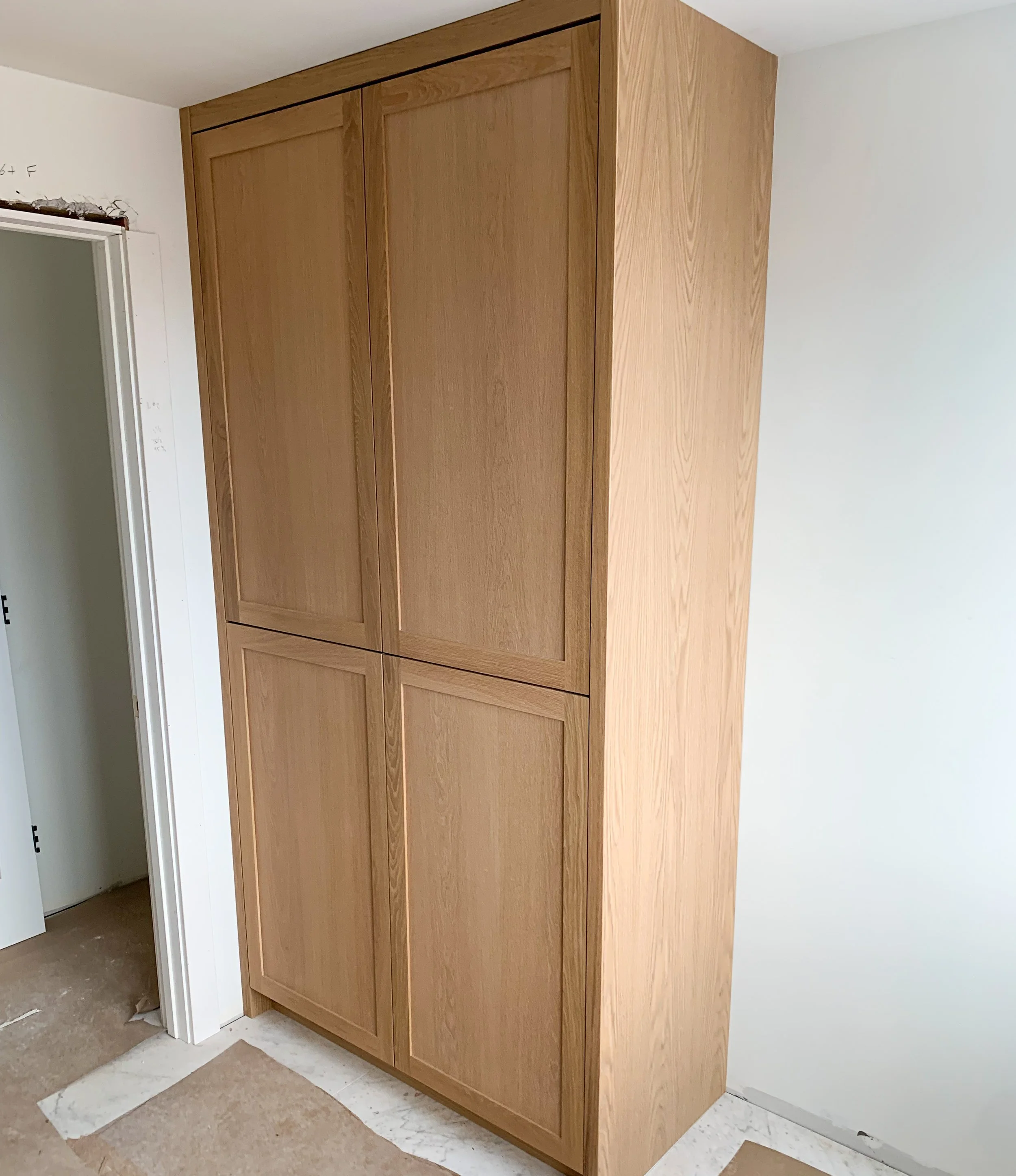 Wooden built-in cabinet next to a door frame in a room under construction.