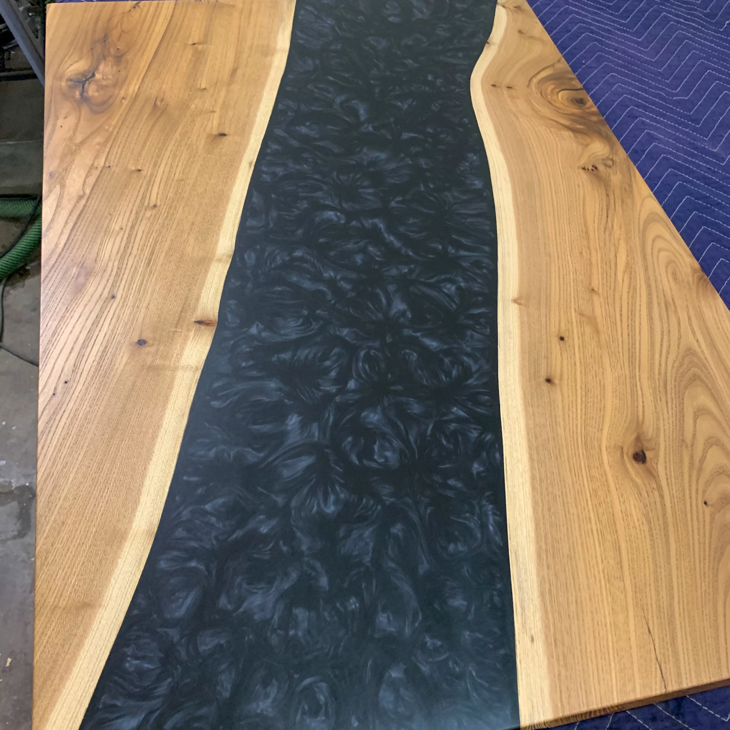 Close-up of a wooden table with a dark, marbled center inlay and a blue cloth partially covering one side.