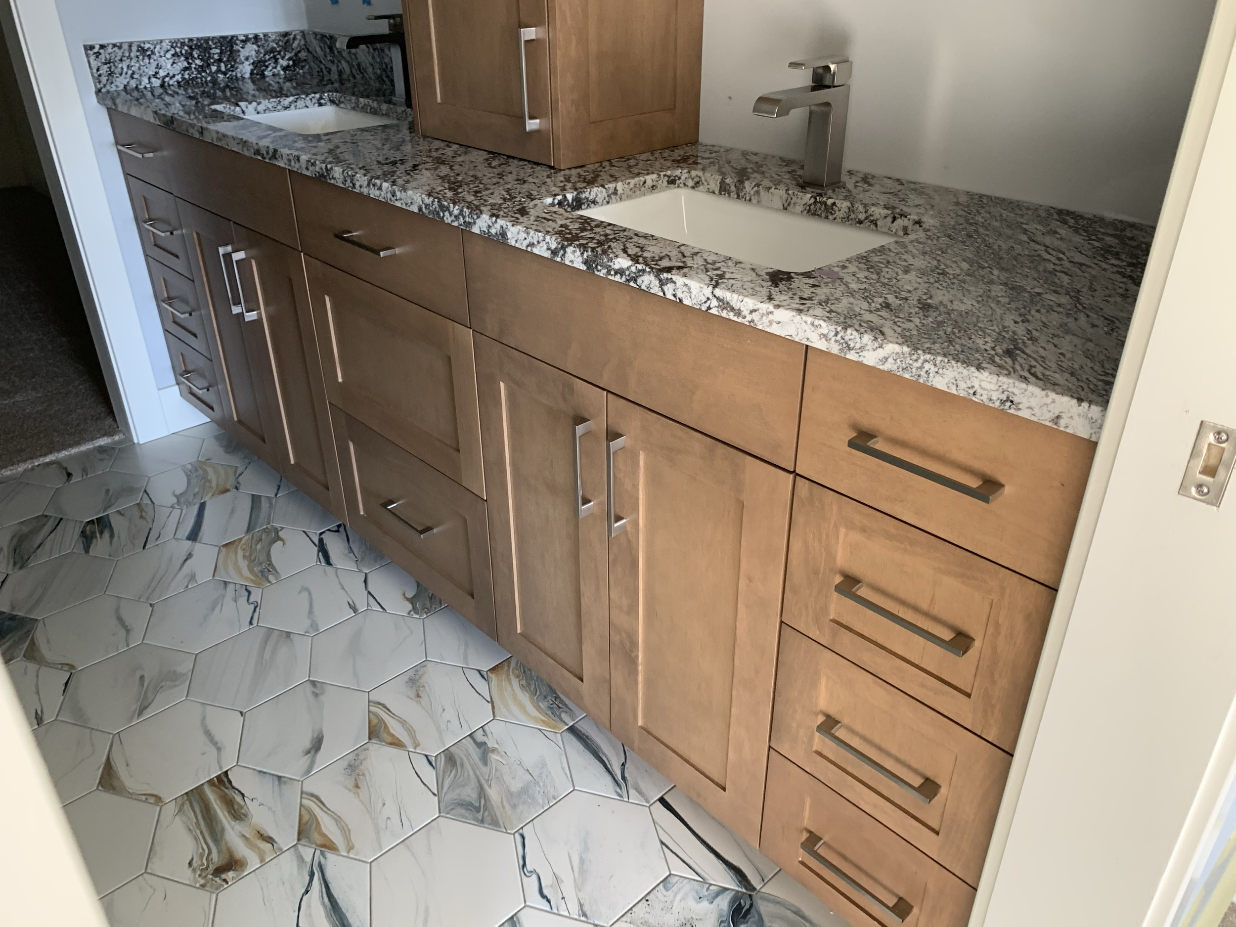 Kitchen cabinet with granite countertop, dual sinks, tile floor with hexagonal marble pattern.