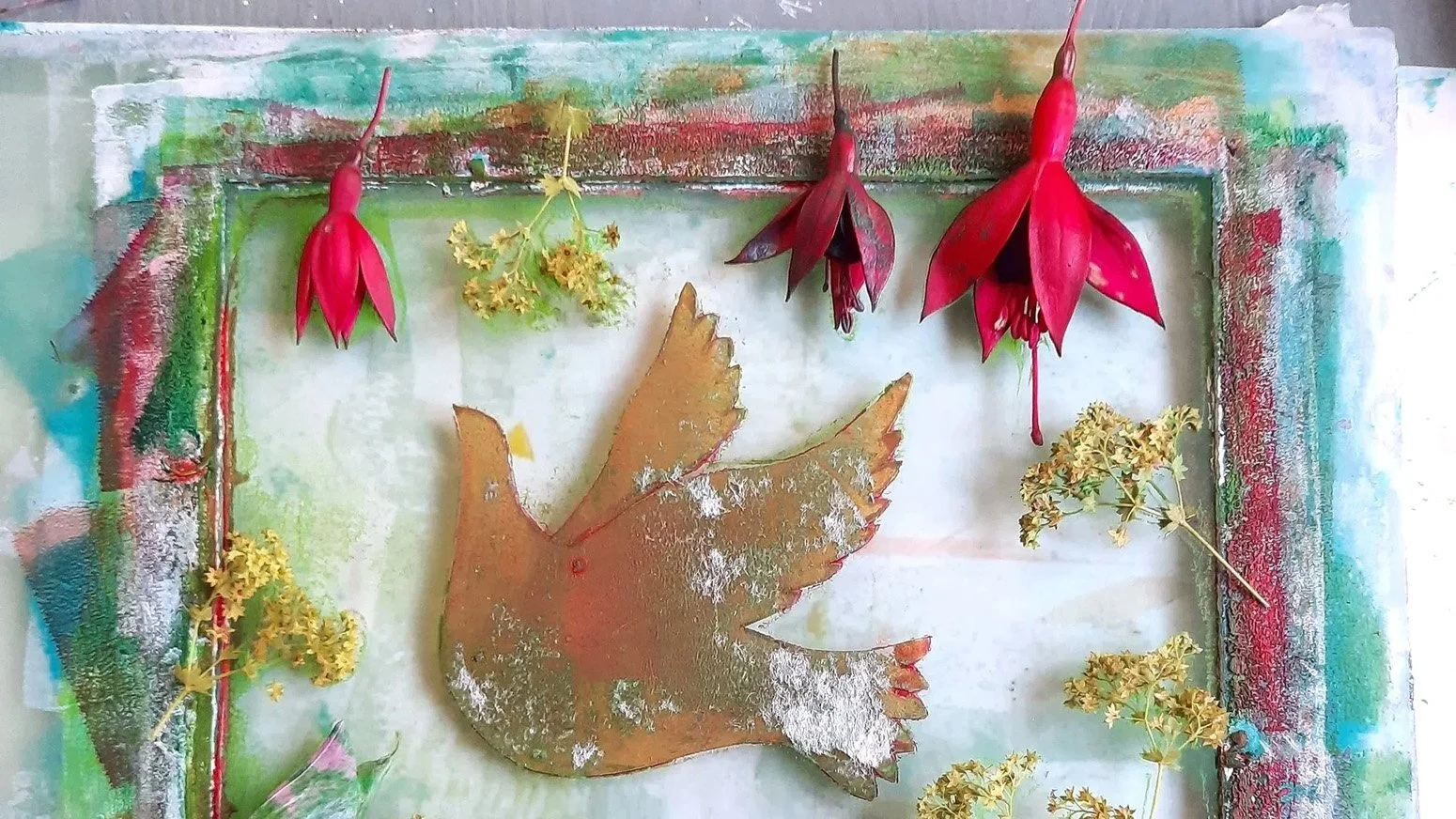 An art piece with dried flowers and a cut-out metal bird on a textured background with multiple colors, including greens, reds, and blues.