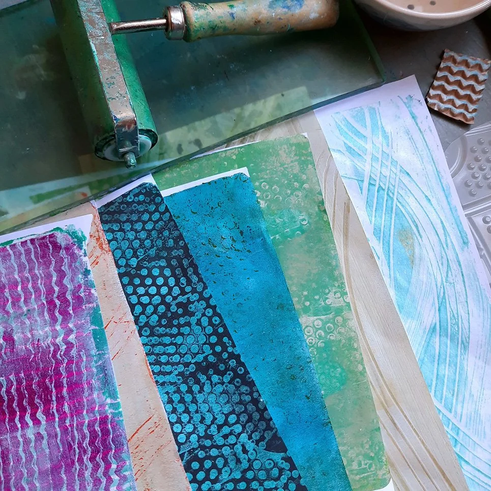 An art workspace with colorful printed papers, a roller tool, and some textured clay pieces.