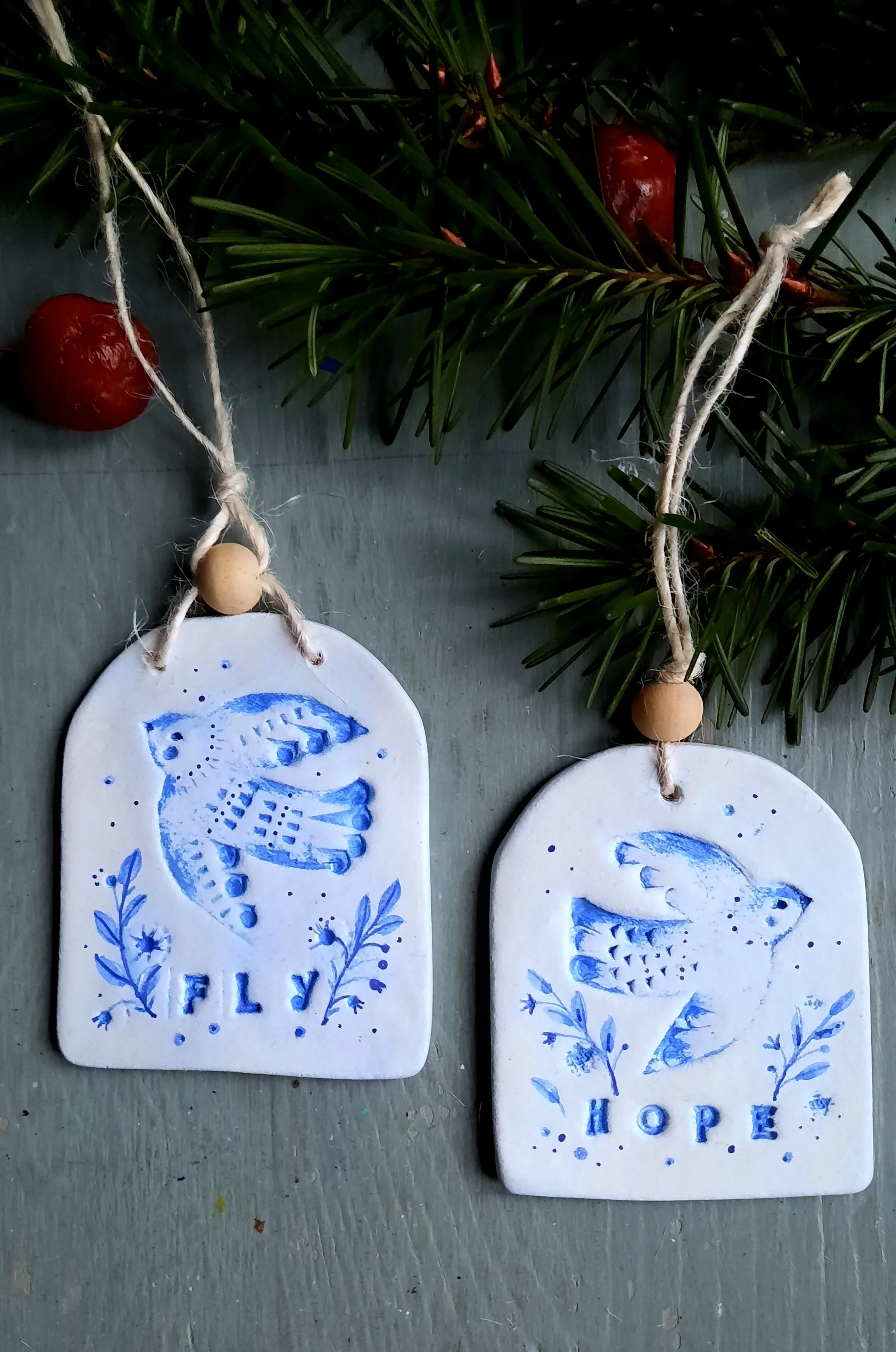 Two clay ornaments featuring a bird each, one with the word ‘Fly’, the other with the word ‘Hope.’