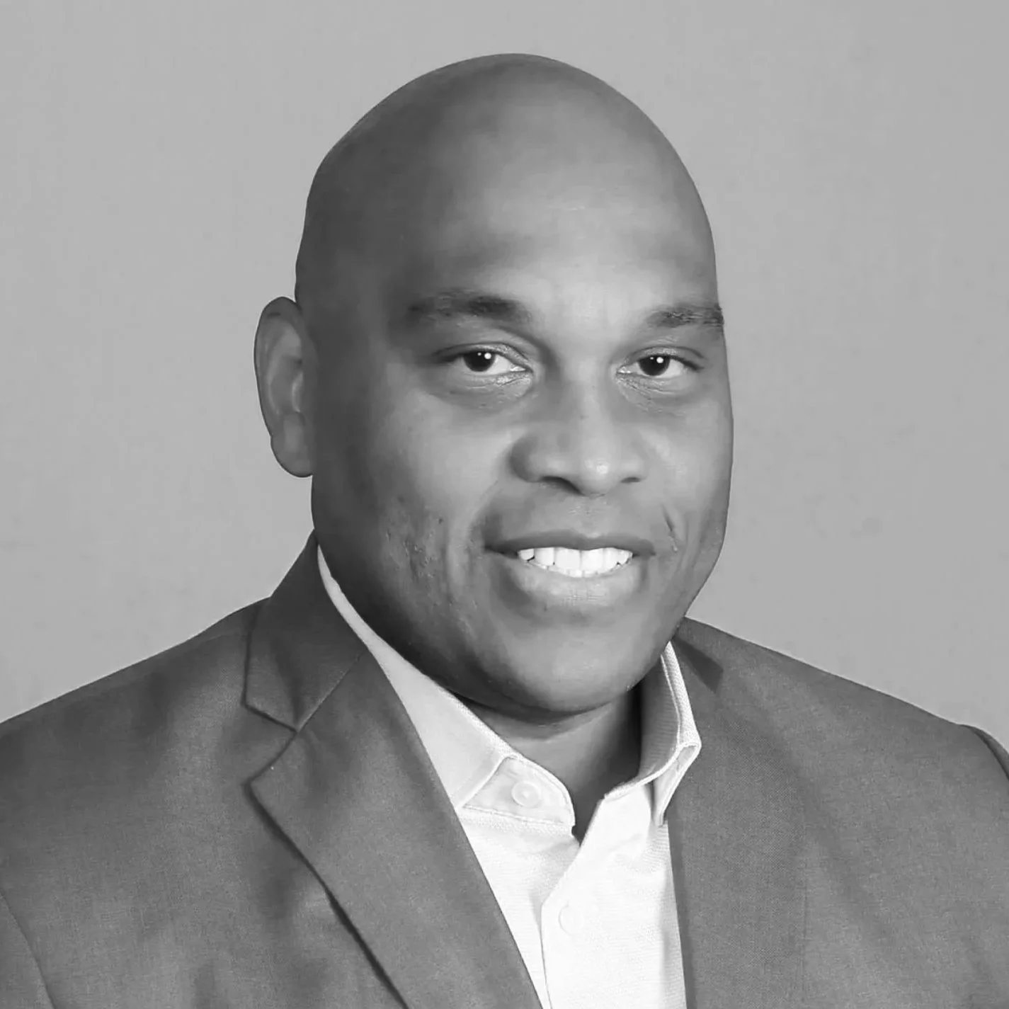 Black and white portrait of a man in a suit, smiling, with a plain background.