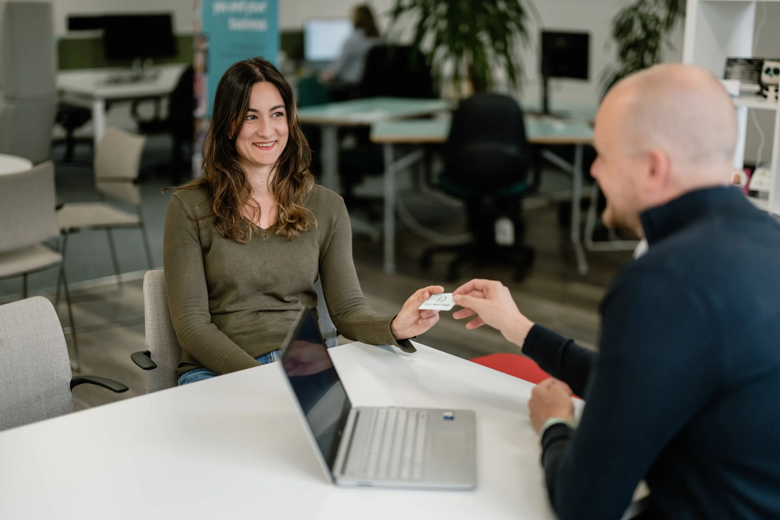 A woman smiling while receiving a business card from a man in an office setting.
