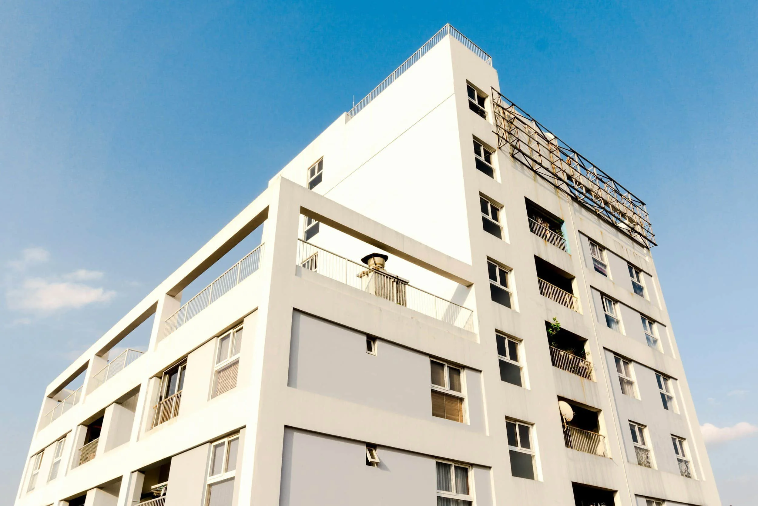 A white modern apartment building with multiple windows and balconies against a bright blue sky.