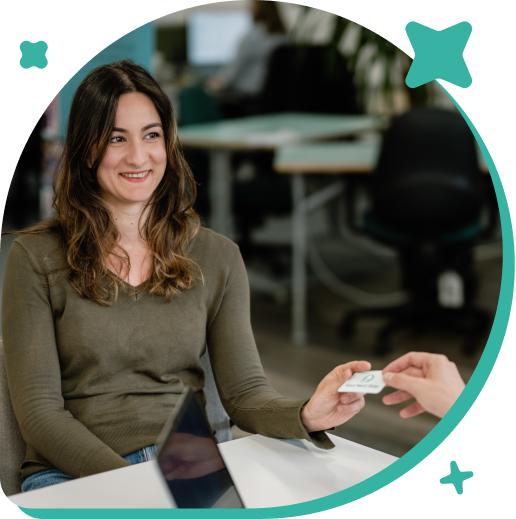 A woman is smiling while handing a business card to someone in an office setting.