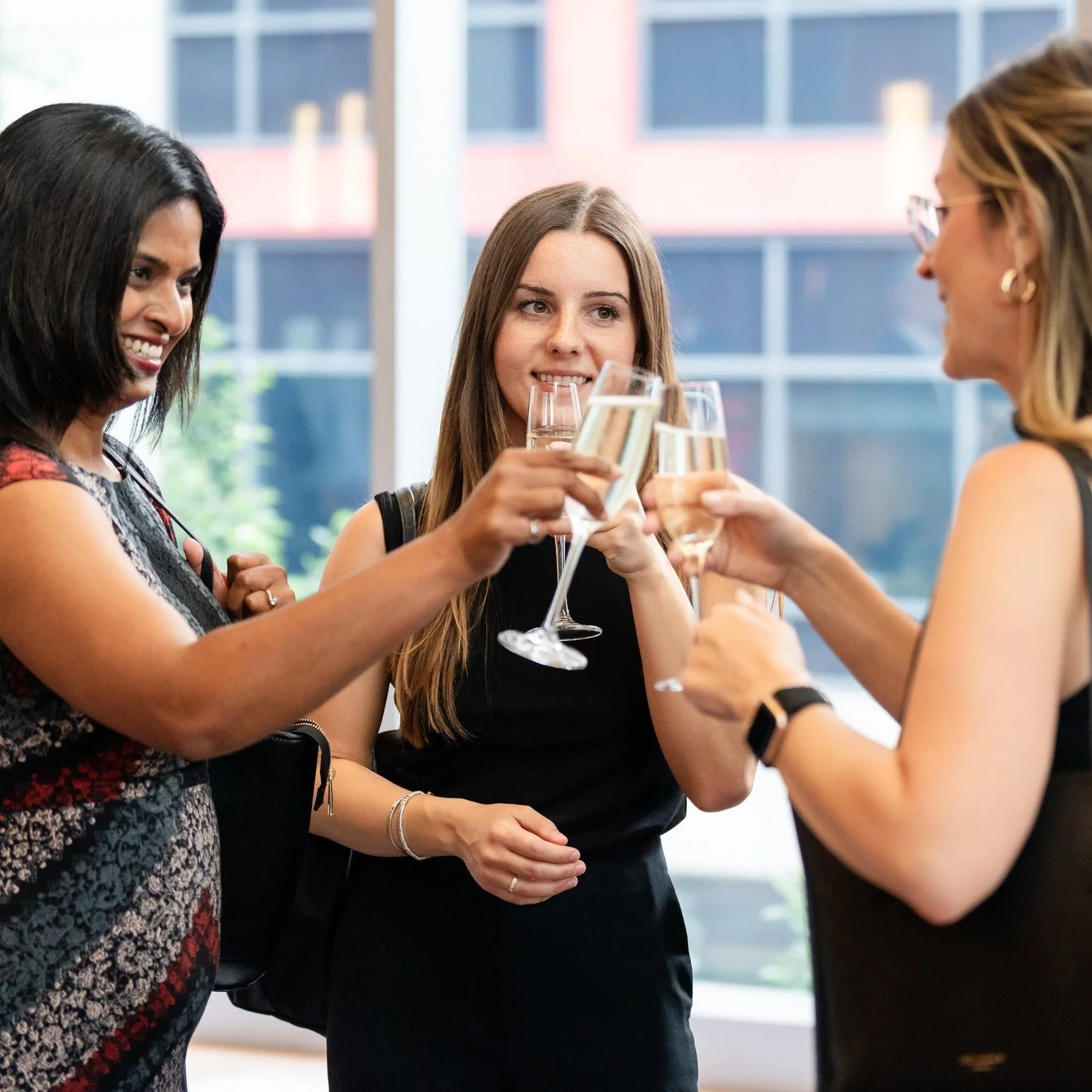 Three women celebrating with champagne glasses, smiling and toasting in a bright room.