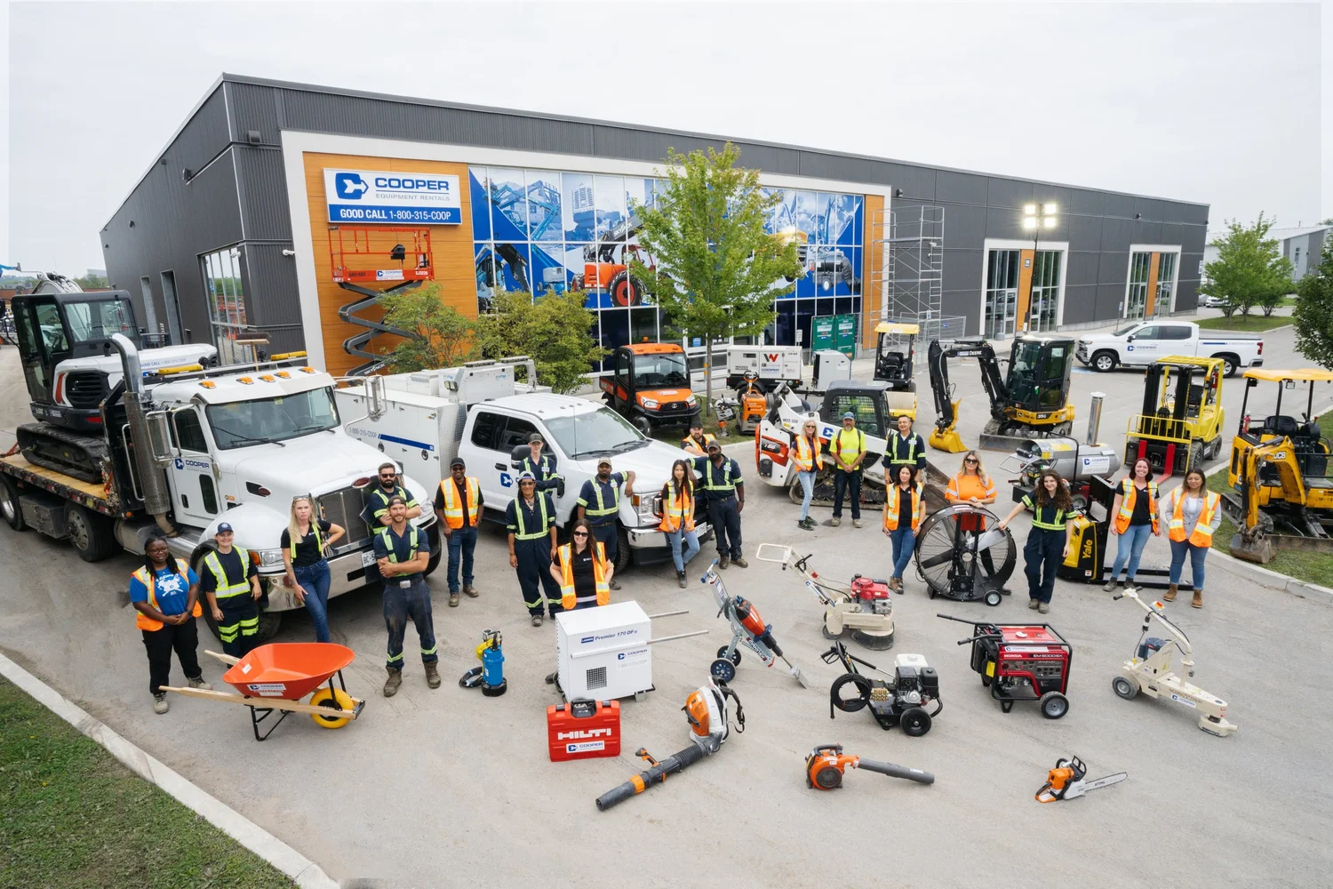 Group of people in safety vests posing with construction equipment and vehicles outside a Cooper Equipment Rentals building.