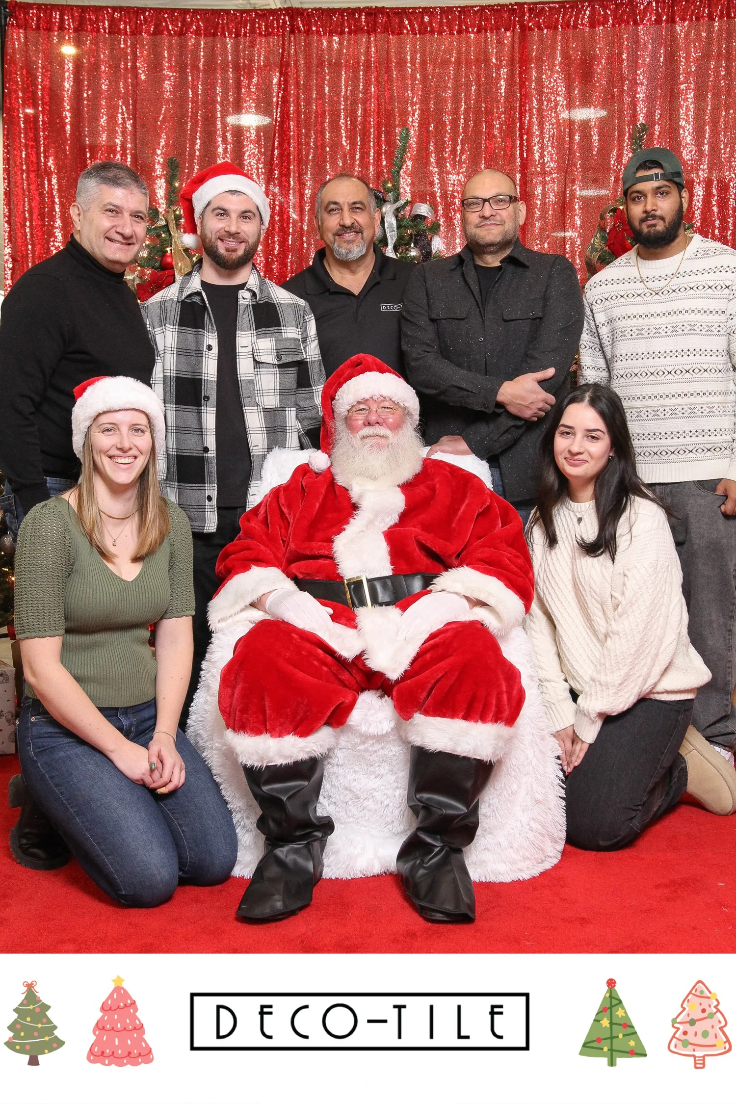 Group photo with Santa Claus and adults wearing festive attire, against a decorated Christmas background. "Deco-Tile" logo displayed at the bottom, along with Christmas tree graphics.