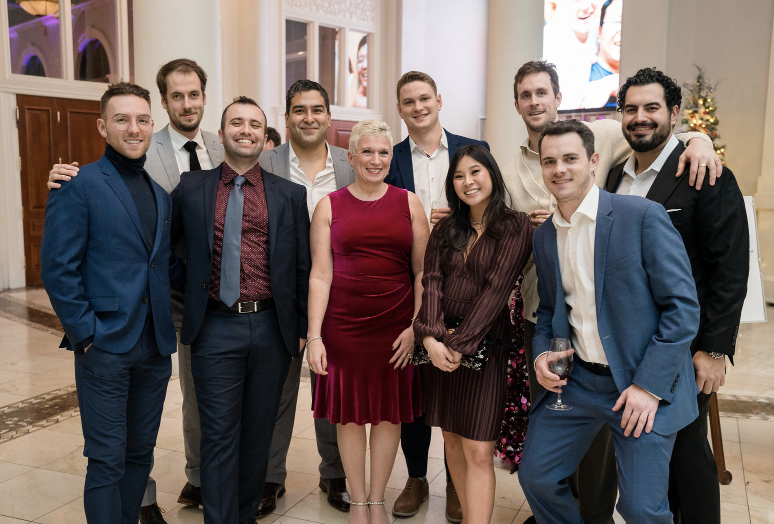 A group of nine people dressed in formal attire posing for a photo at a social event in an elegant indoor venue.