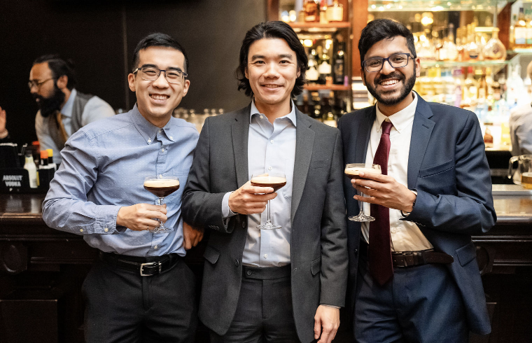Three men in business attire holding cocktails in a bar.