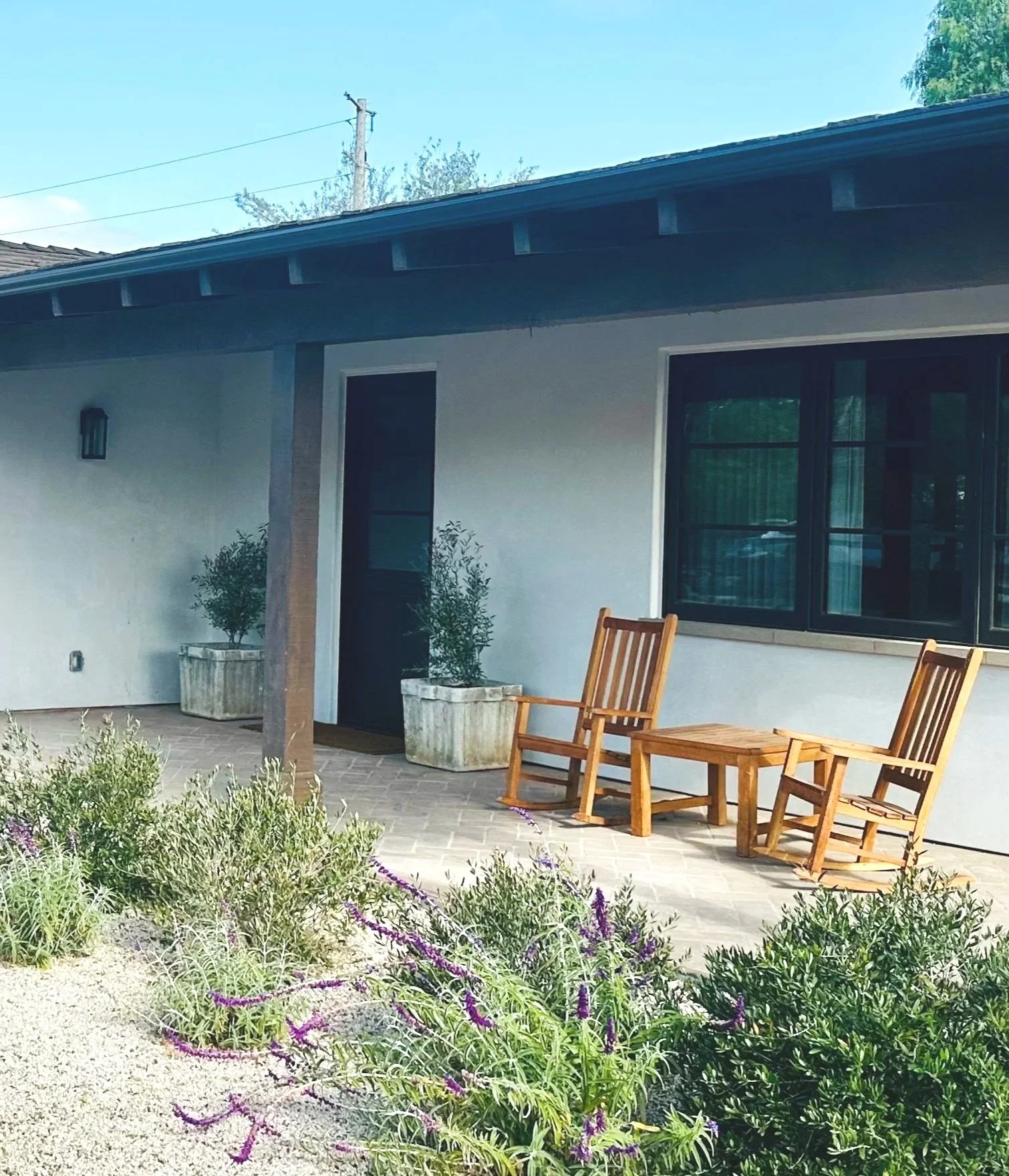 Charming front porch on a Rancho Santa Fe horse farm looks luxurious with French limestone planters filled with olive trees, lavender, sages, Olives, rocking chairs, and soft warm grey gravel. outdoor luxury by krista Percival Landscape Design