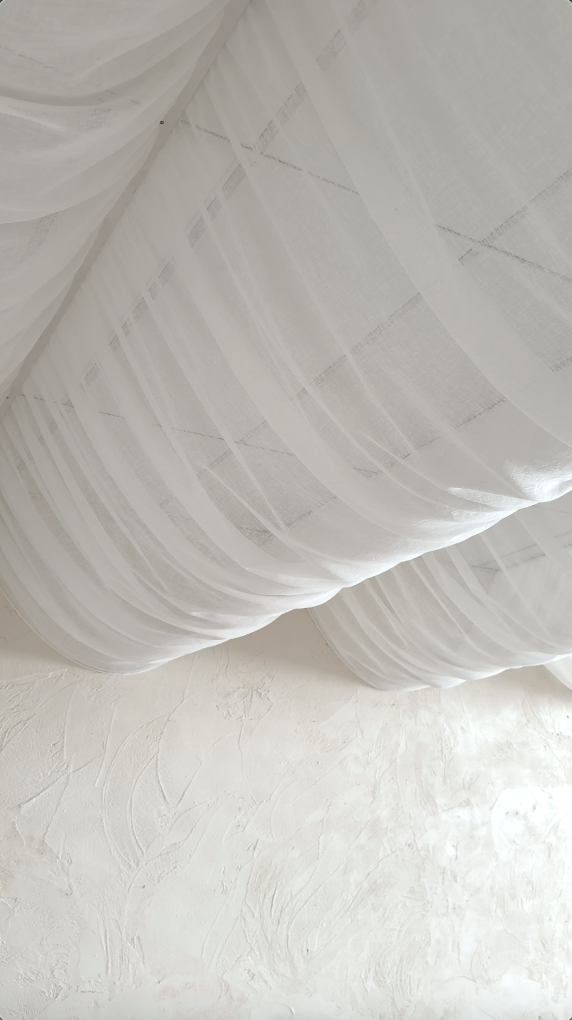 Close-up of white sheer curtains hanging in front of a textured white wall.