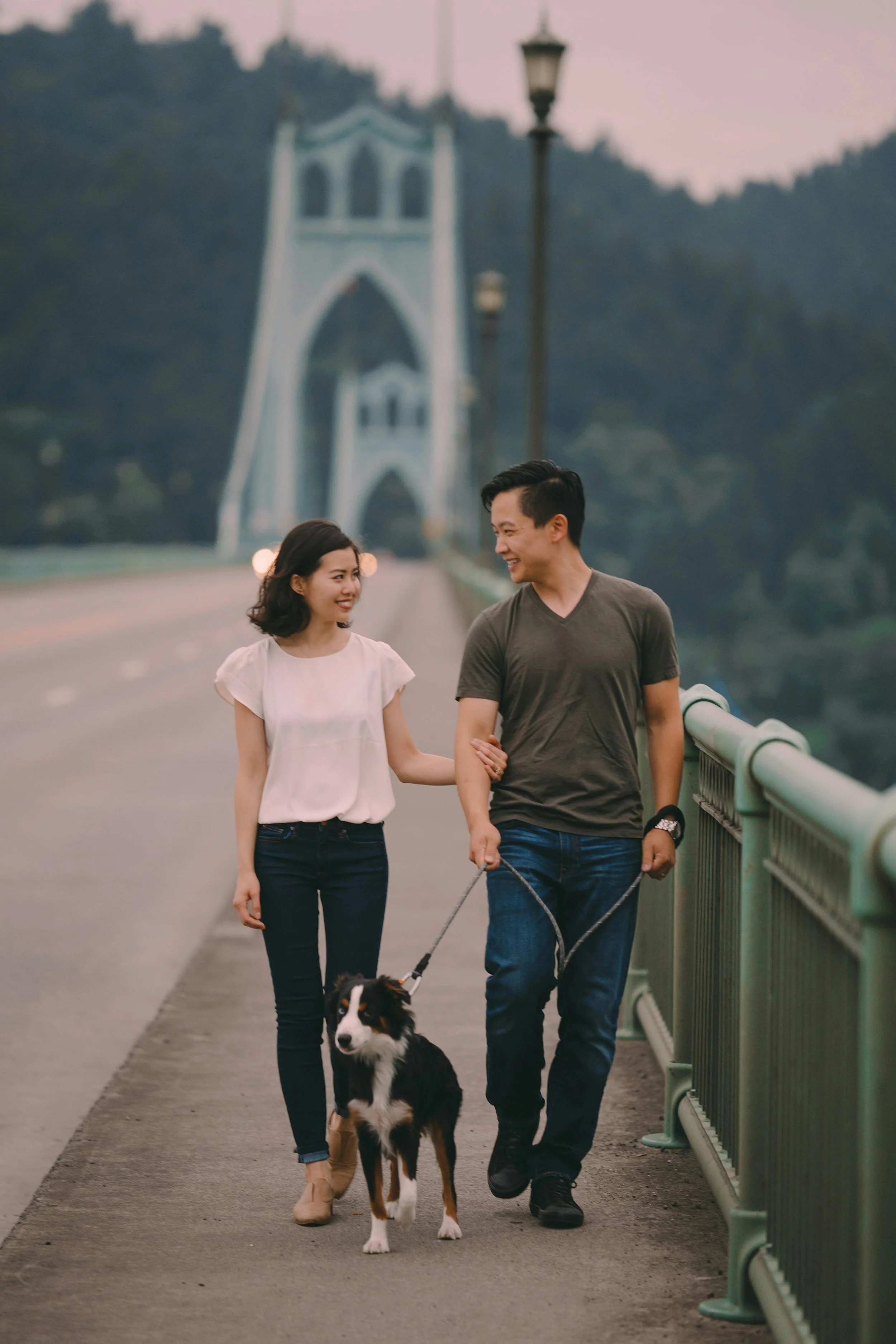 Two pet parents walk a leashed dog across a bridge.